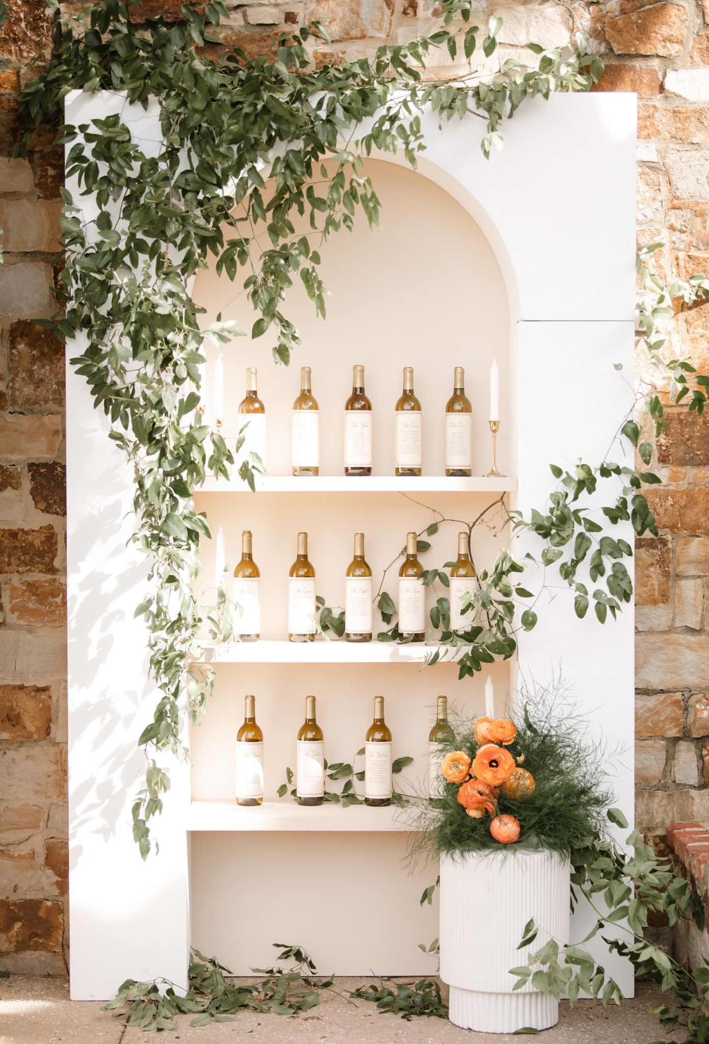 Elegant wedding bar display with hanging gold pendant lights and orange floral accents against a stone wall.