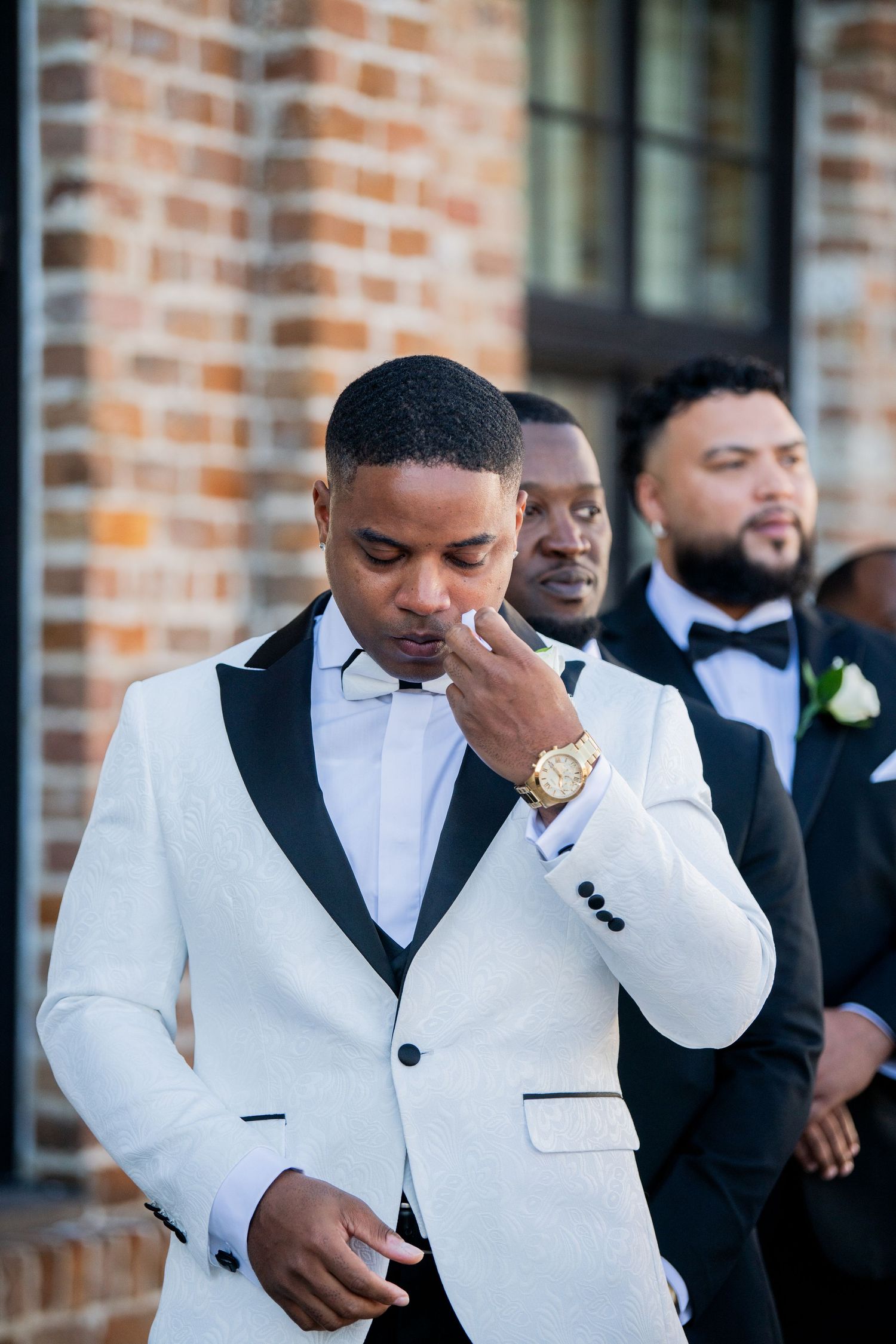 A touching pre-wedding moment with groomsmen against a brick backdrop.