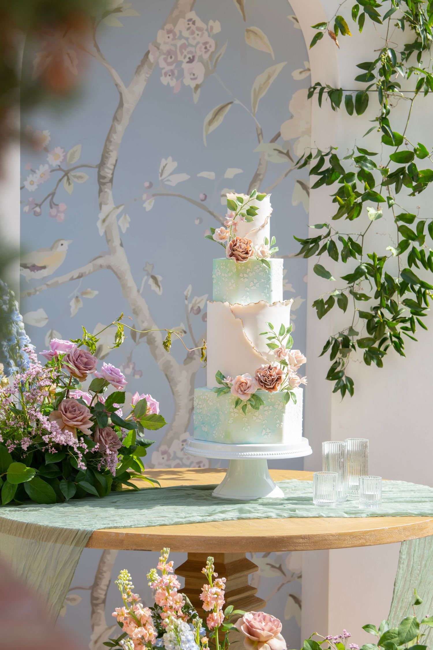 Wedding cake display table with floral decorations and delicate branch wall art.