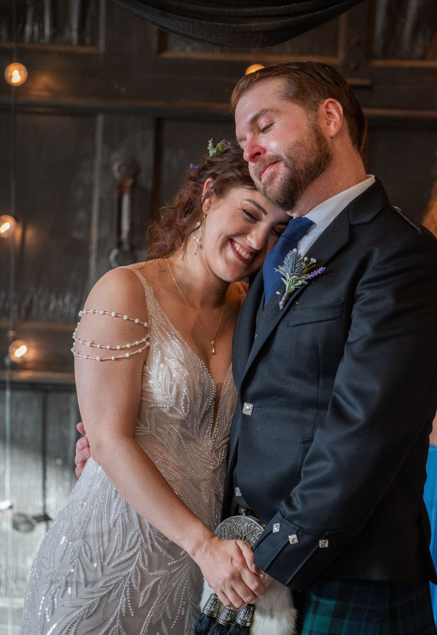 Tender moment between newlyweds in rustic venue with ambient lighting.