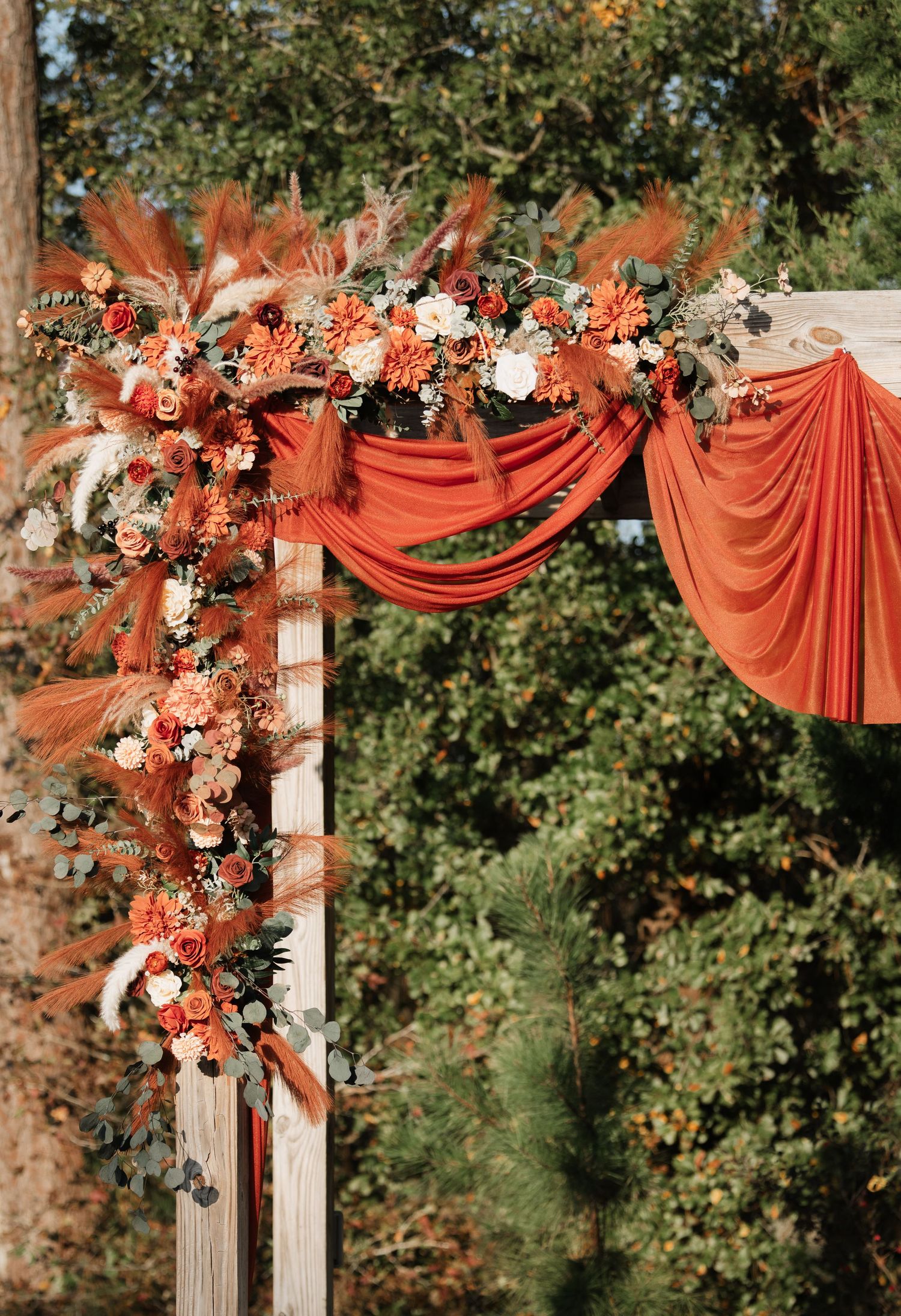 Outdoor wedding arch decorated with coral draping fabric and white floral arrangements.