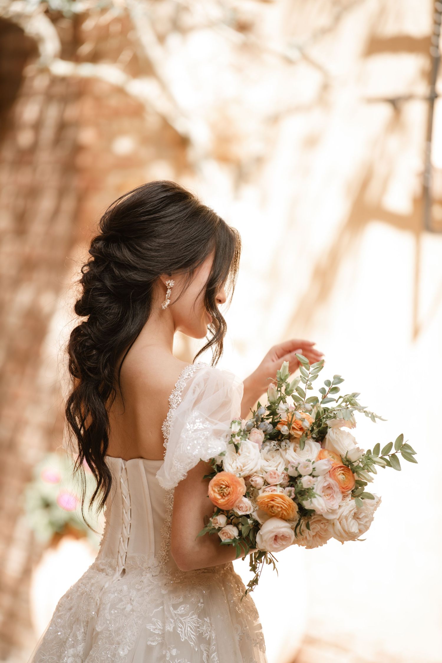 Romantic bridal portrait featuring a lace wedding dress and peach-toned bouquet in soft sunlight.