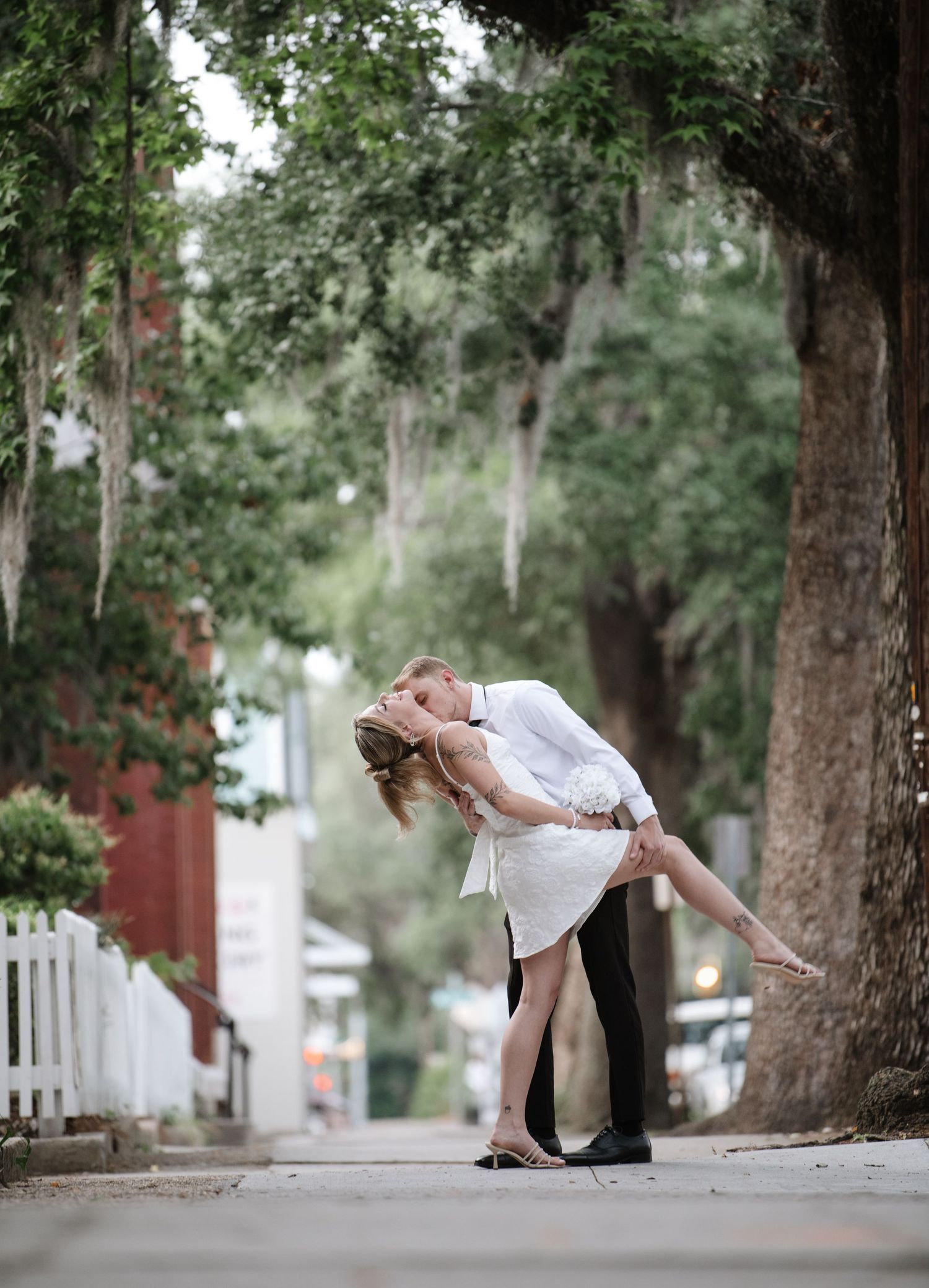Elegant dip pose during wedding photoshoot on tree-lined path.