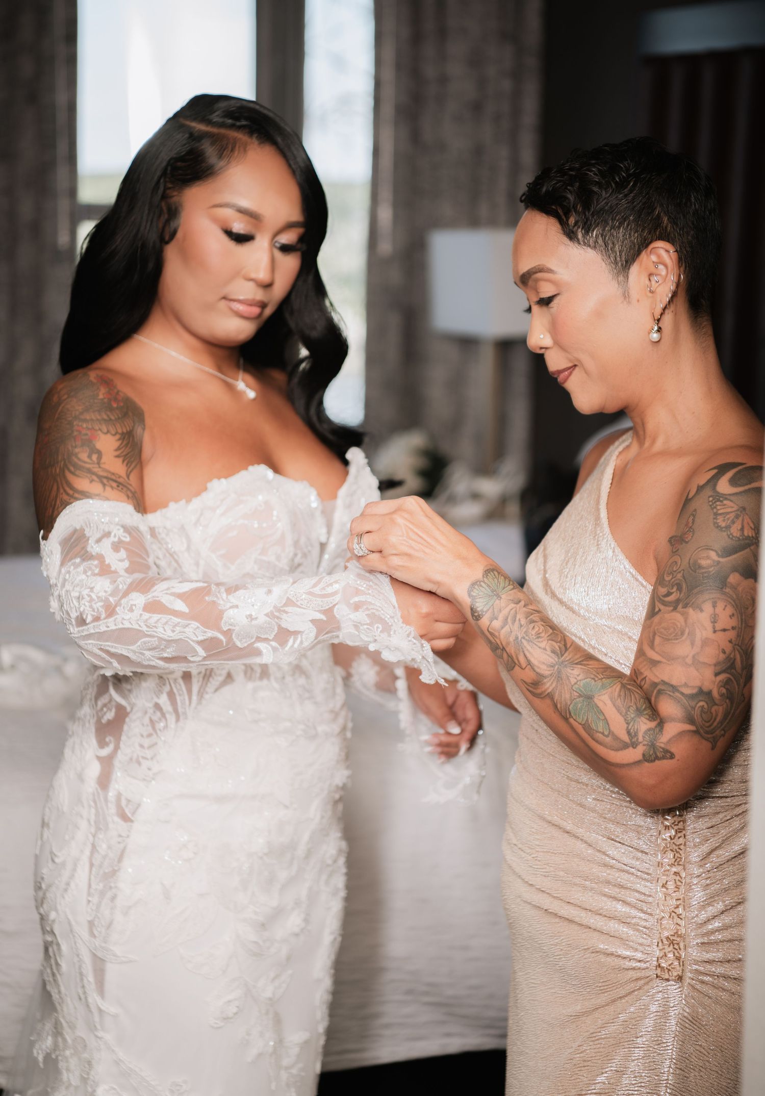 Two people wearing white and champagne colored dresses pose together in an emotional moment.