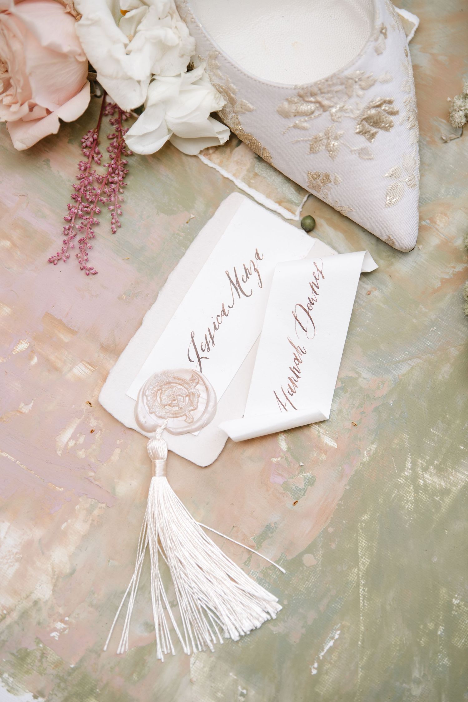 Elegant wedding place cards with white tassels and calligraphy on a distressed green surface.