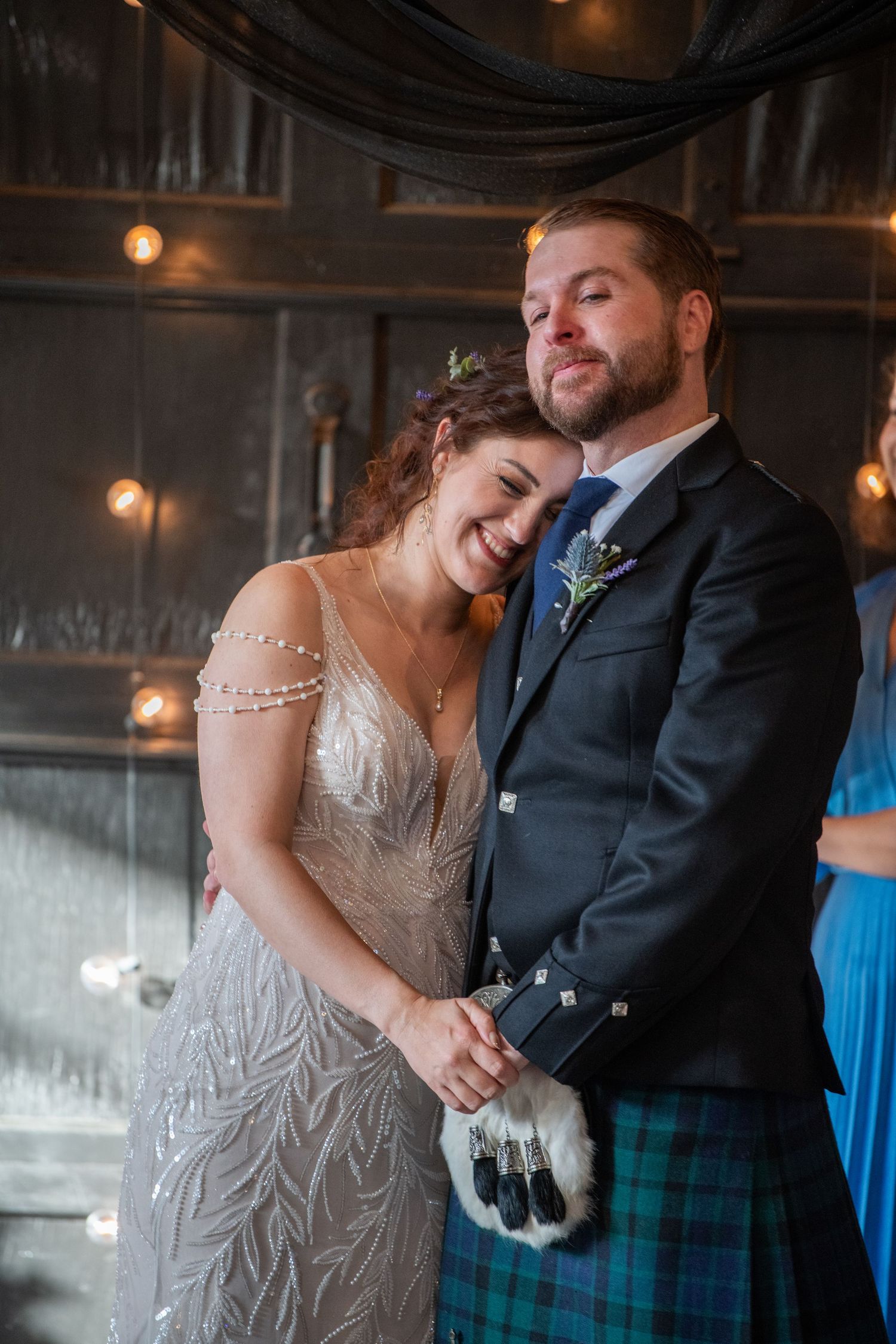 Intimate wedding moment in industrial venue with string lights and dark decor.