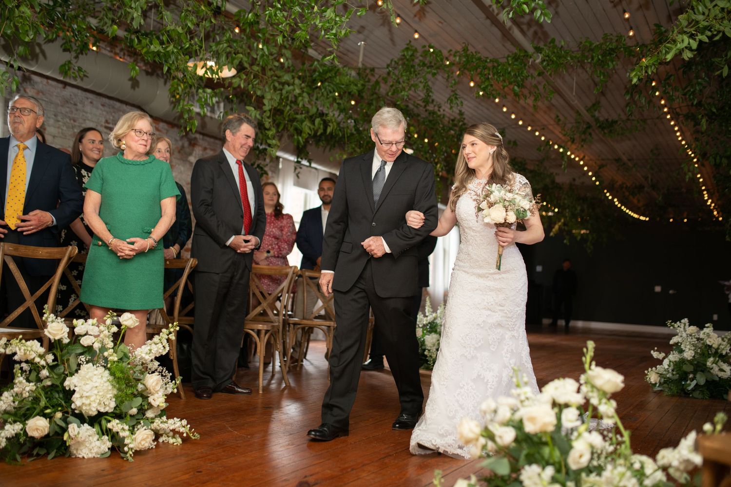 Indoor wedding venue decorated with hanging greenery, white flowers and wooden chairs.
