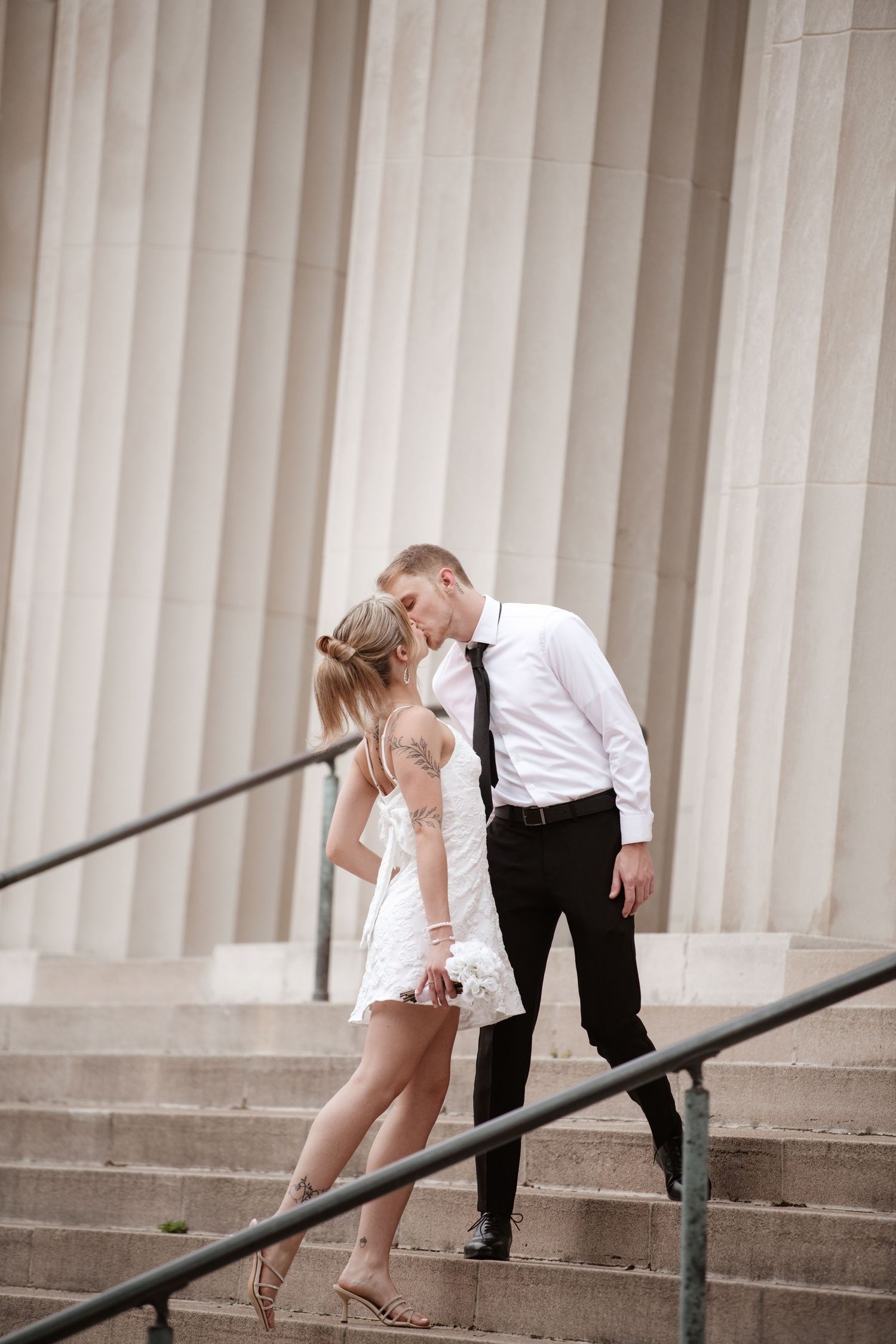 Couple shares romantic moment on classical stone steps with columns.