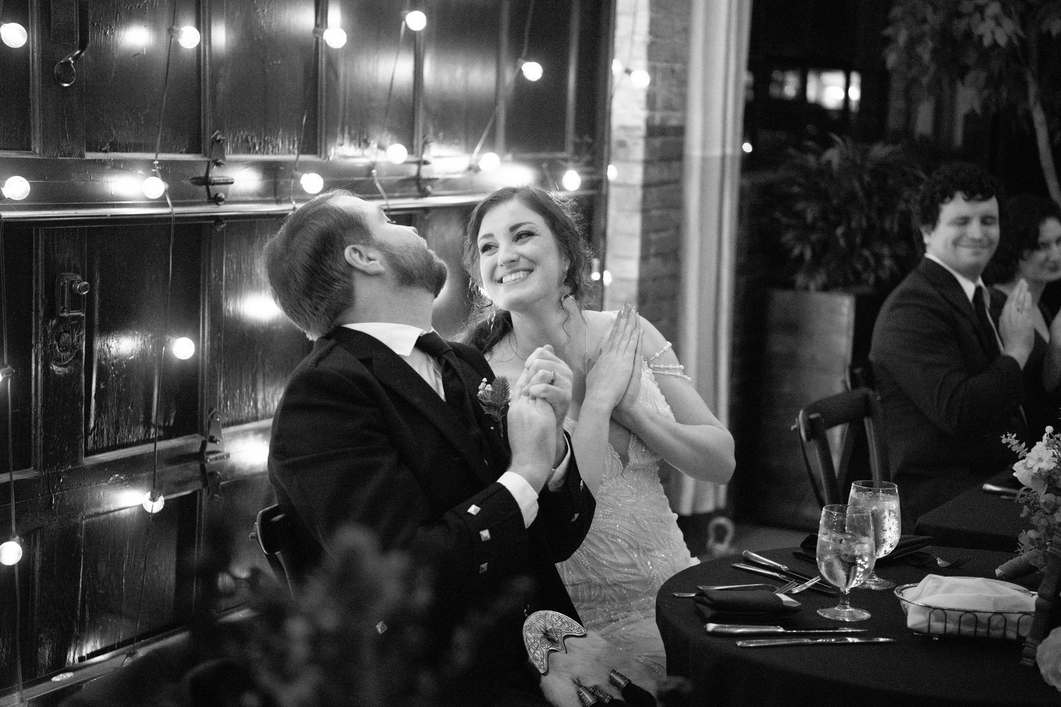 Evening wedding reception with string lights and guests enjoying conversations at tables.