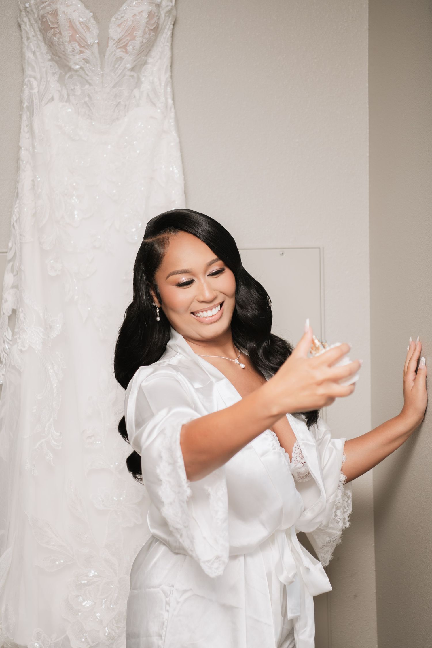 Joyful wedding morning preparation scene with white lace dress in background.