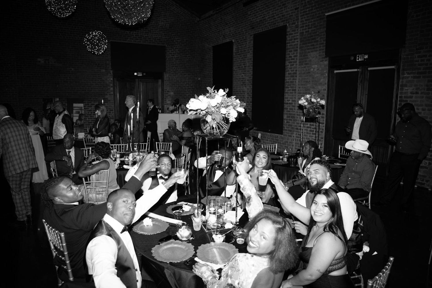 Black and white photo of wedding reception guests celebrating at decorated tables.