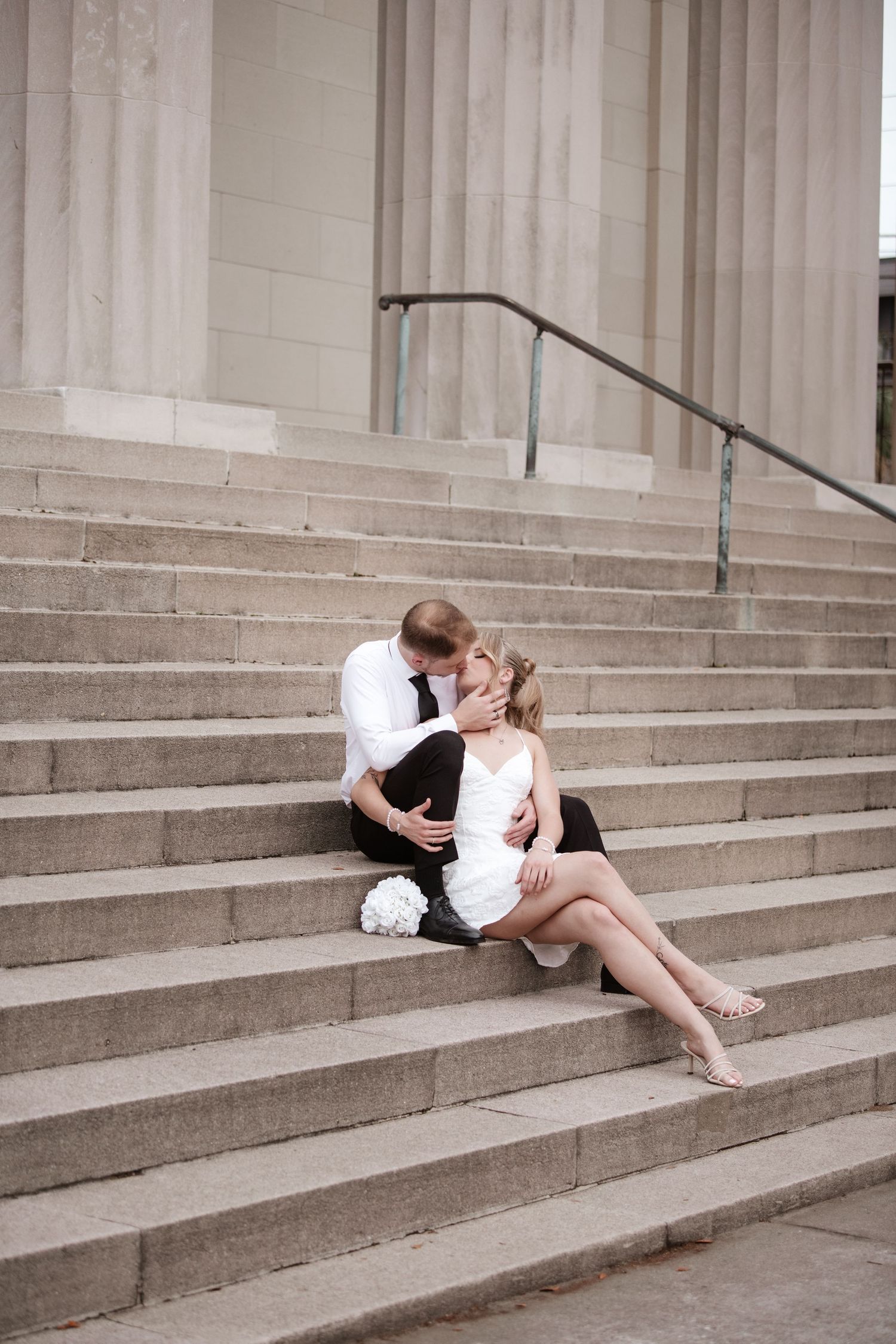 A couple shares a tender moment while resting on grand outdoor steps.