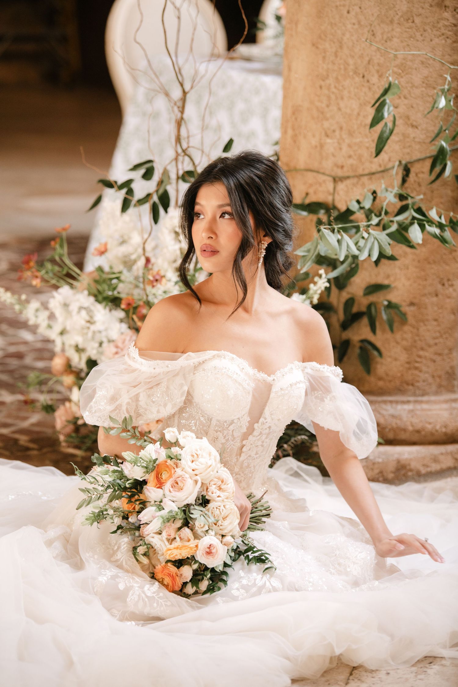 Romantic bridal portrait with peach and white floral bouquet in a stone colonnade setting.