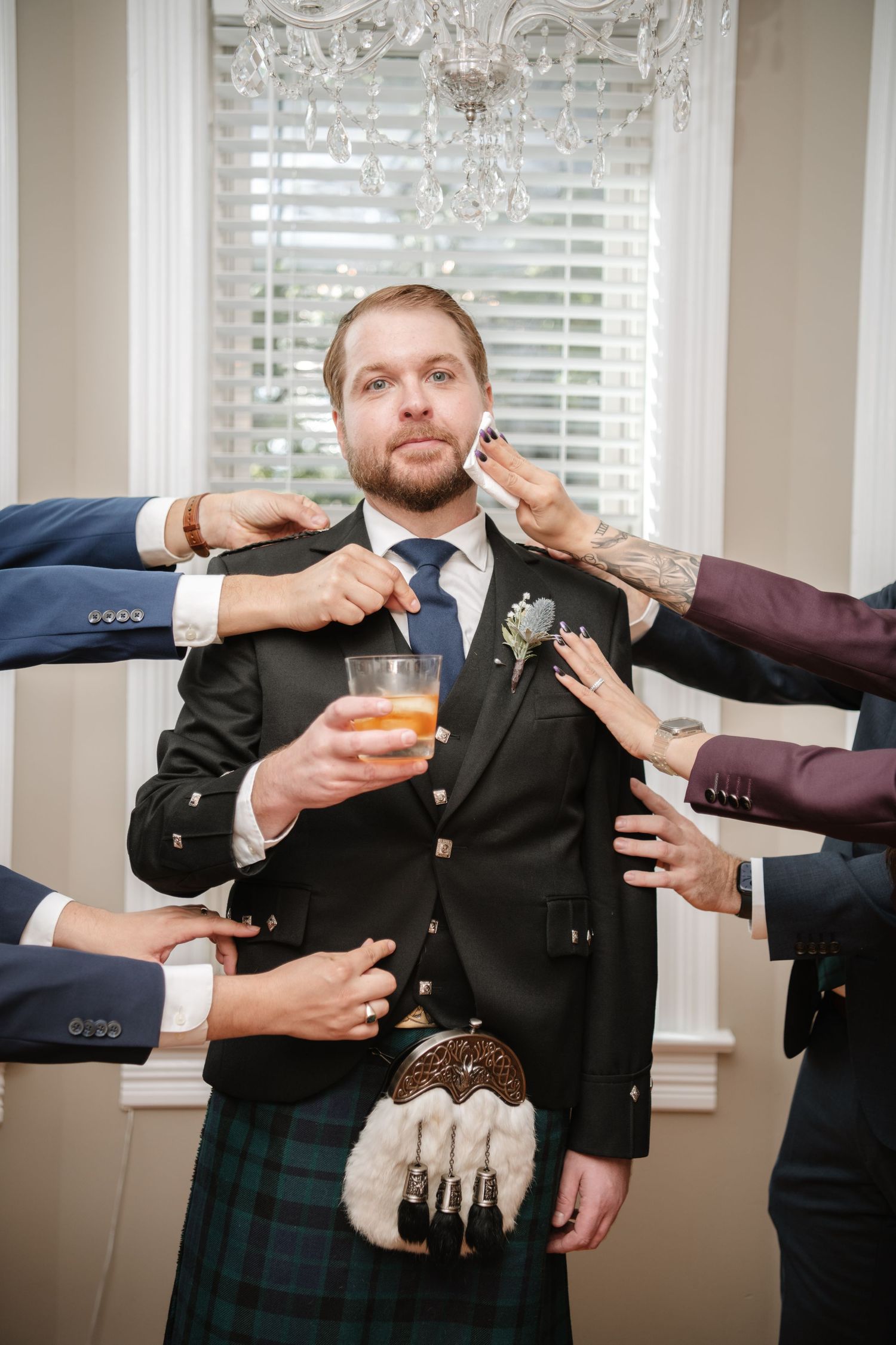 Multiple hands reach to adjust formal attire while holding drinks during preparation.