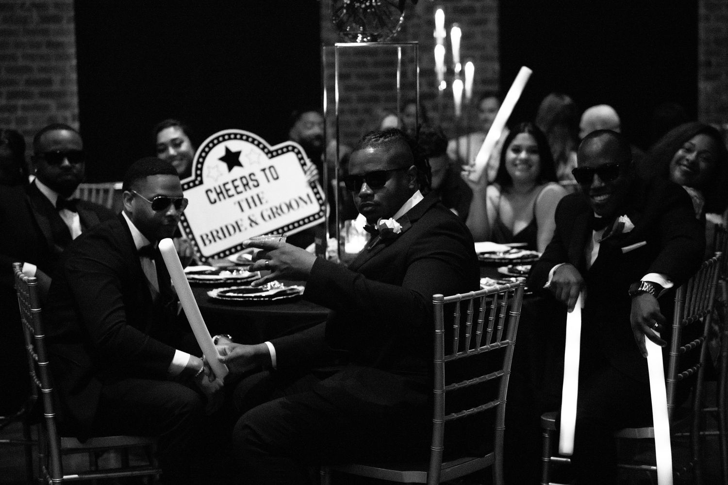 Black and white photo of wedding guests celebrating with props at reception.