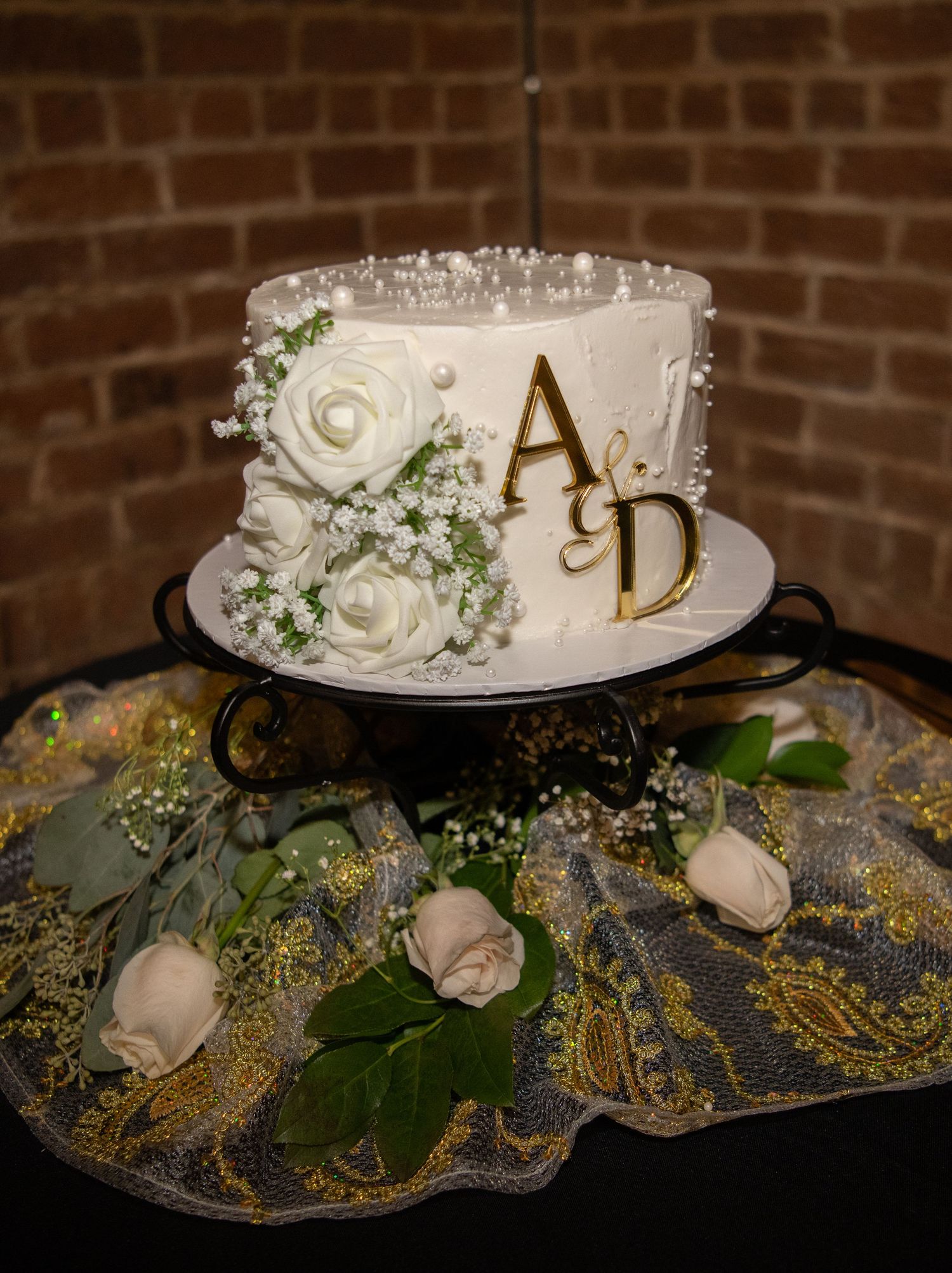 White wedding cake decorated with roses and gold accents on an ornate display.