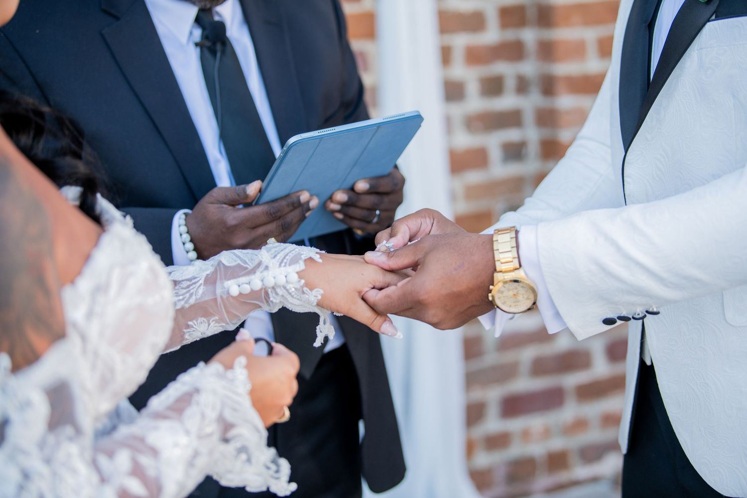 Multiple shots of hands exchanging rings against a brick wall background.