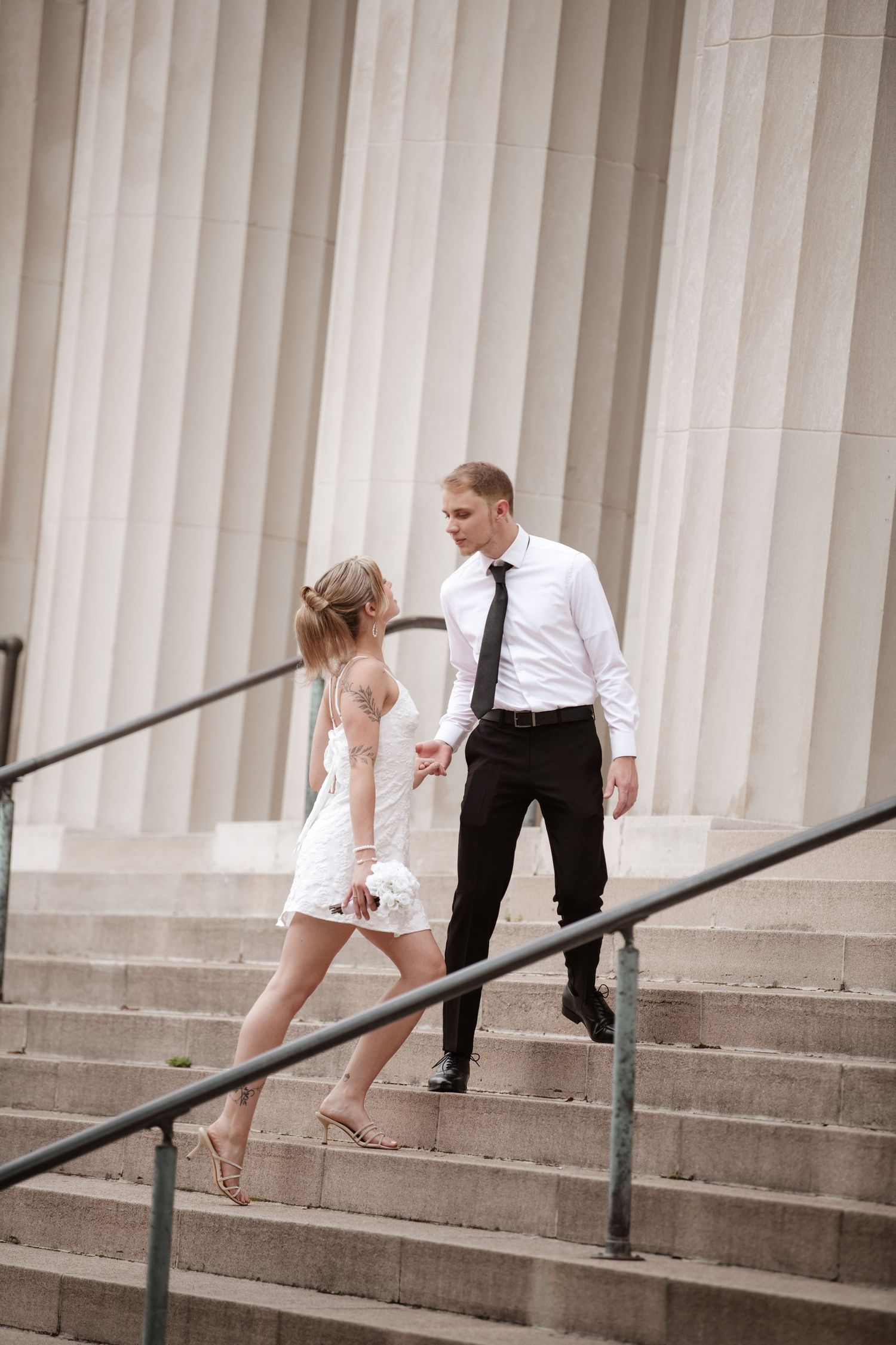 Couple descends stone steps with white columns in a romantic sequence.