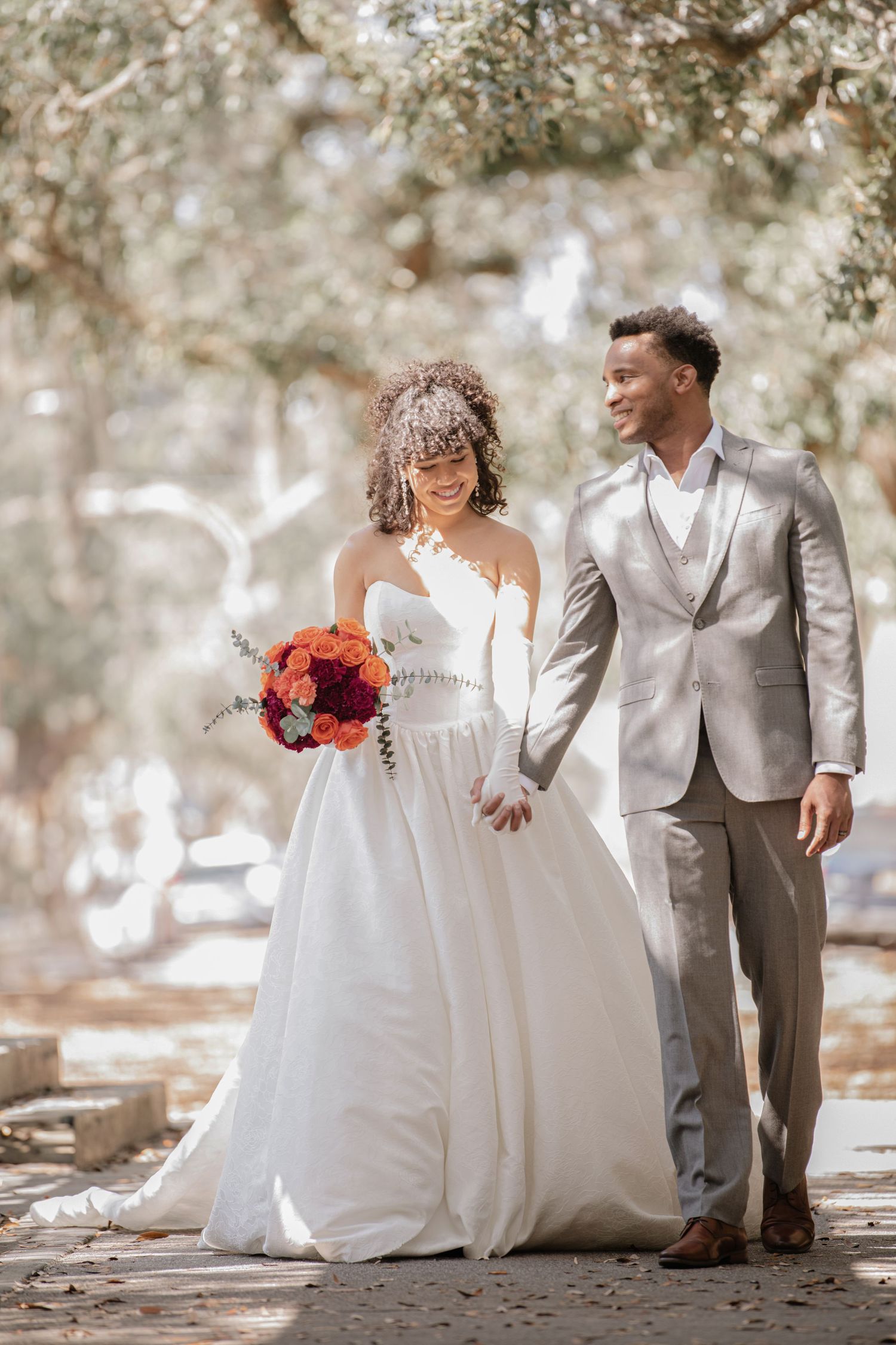 Wedding couple in white and grey attire pose together in a dreamy outdoor setting.