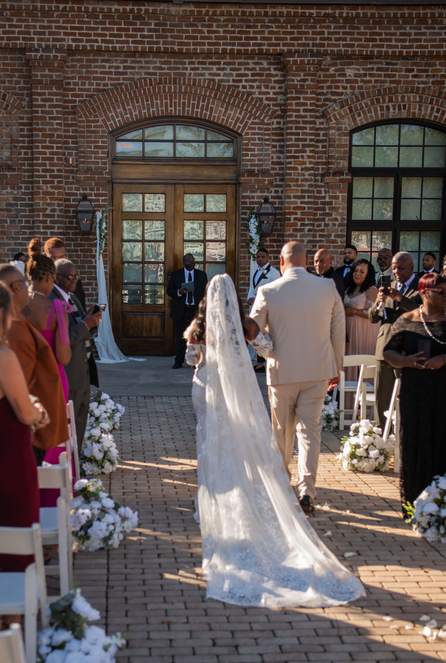 Outdoor wedding ceremony with white floral decorations against brick building backdrop.