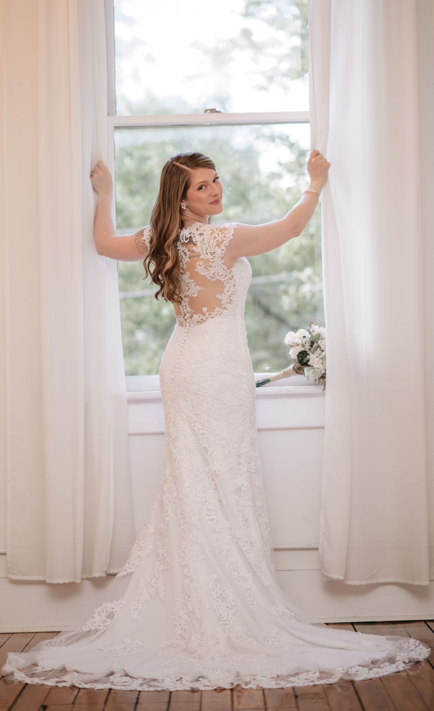 Back view of lace wedding gown with sheer details against bright window.