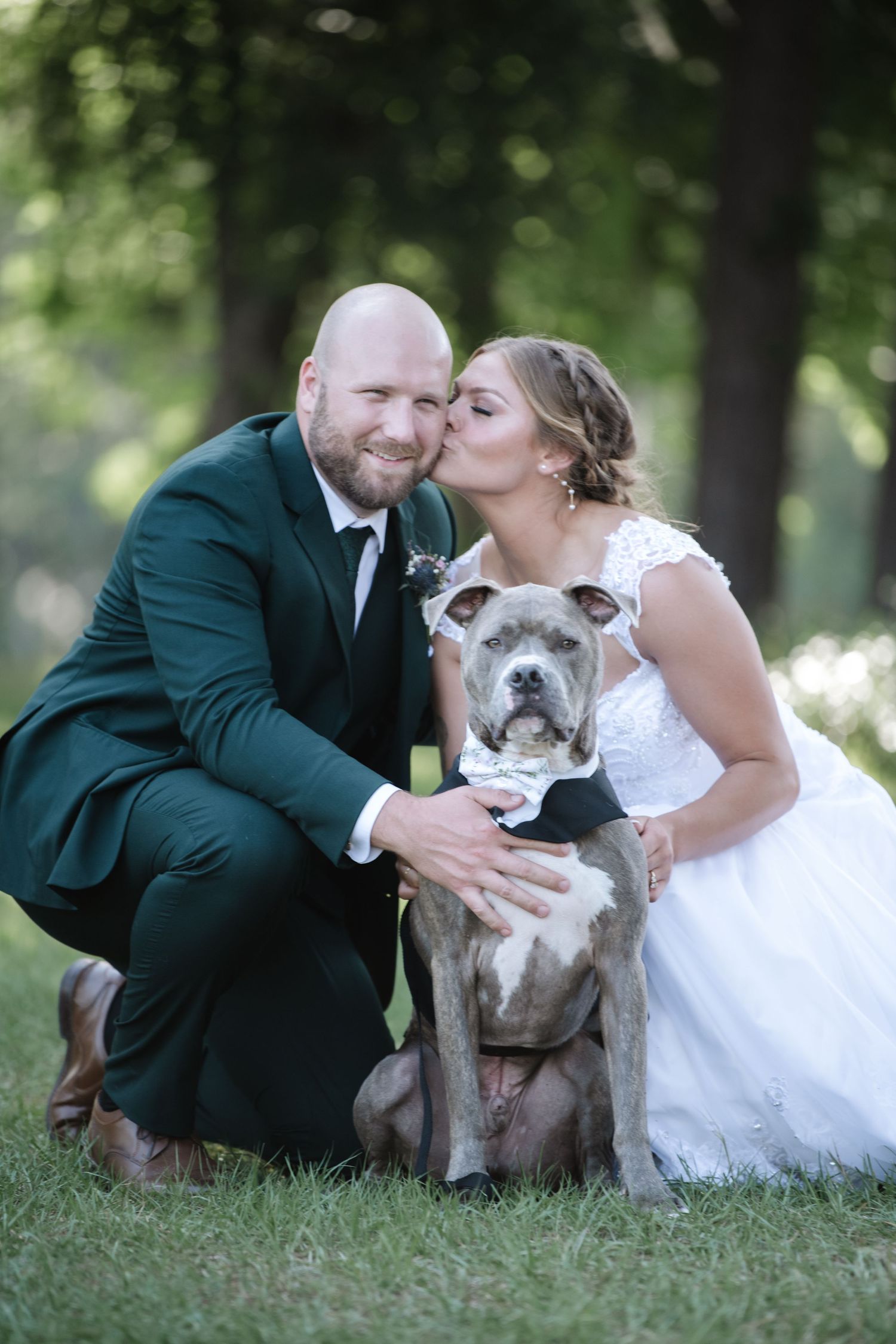Newlyweds posing with their bulldog on grass during wedding portraits.