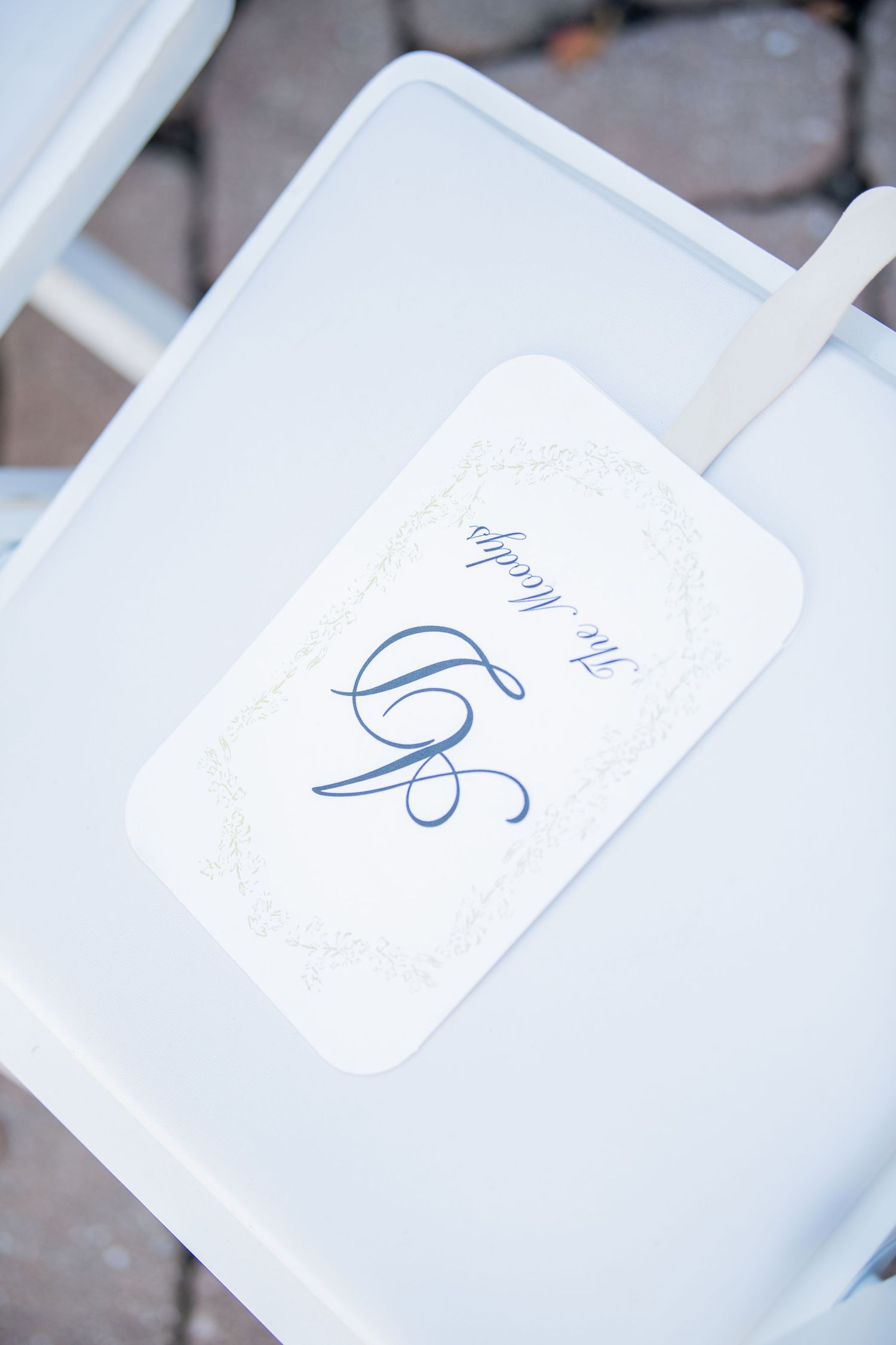 White folding chair with elegant blue monogram label at wedding venue.