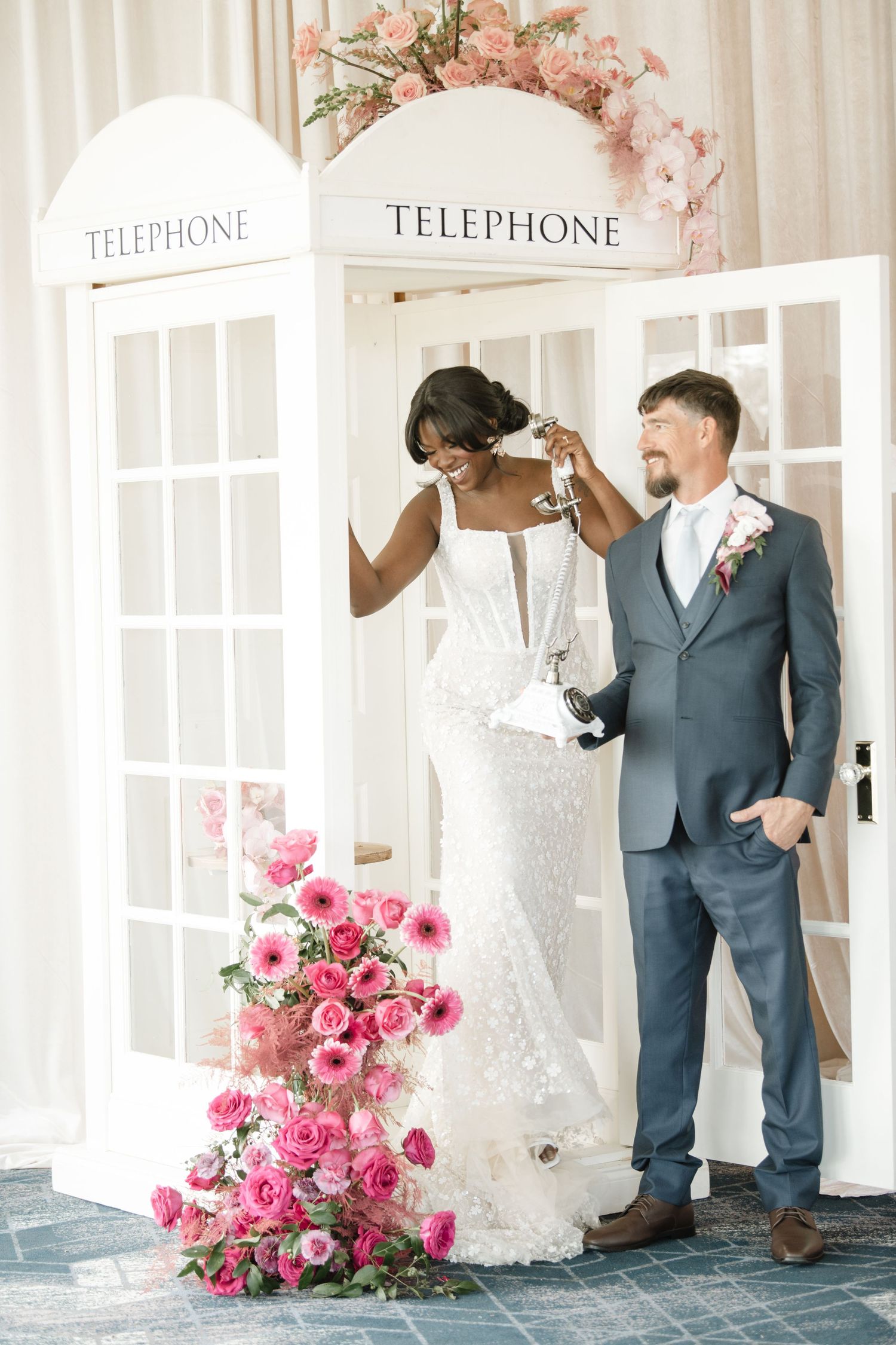 Wedding photo shoot setup with vintage telephone booth and pink floral arrangements.