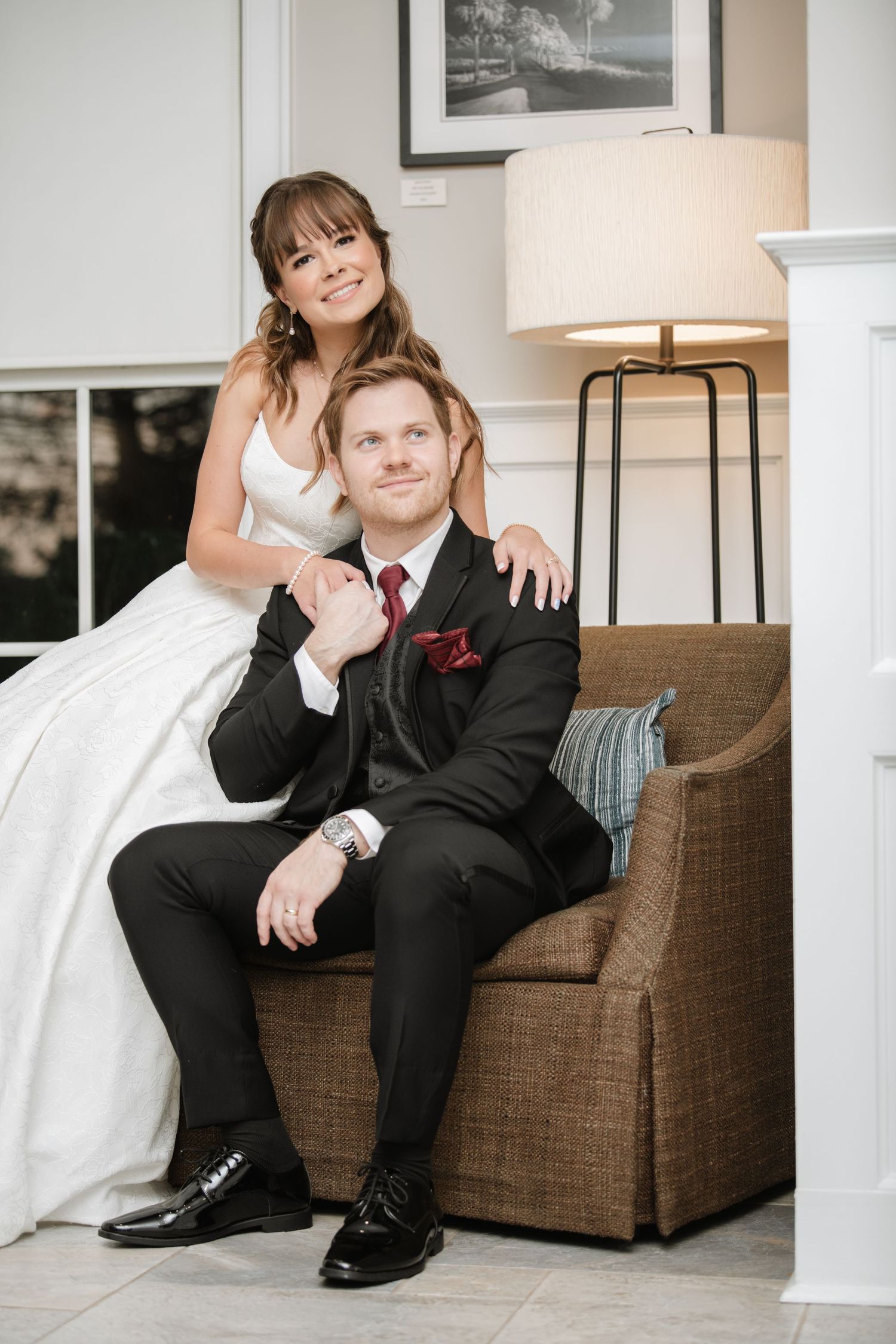 Wedding couple sits together on brown couch, showing close-up details of formal attire and intimate moments.