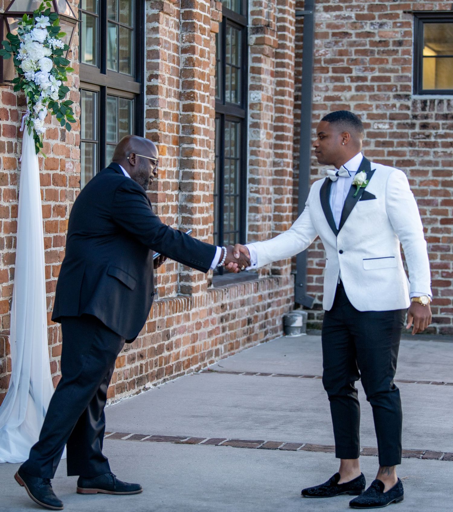 Wedding party members in formal attire posing along brick wall exterior.