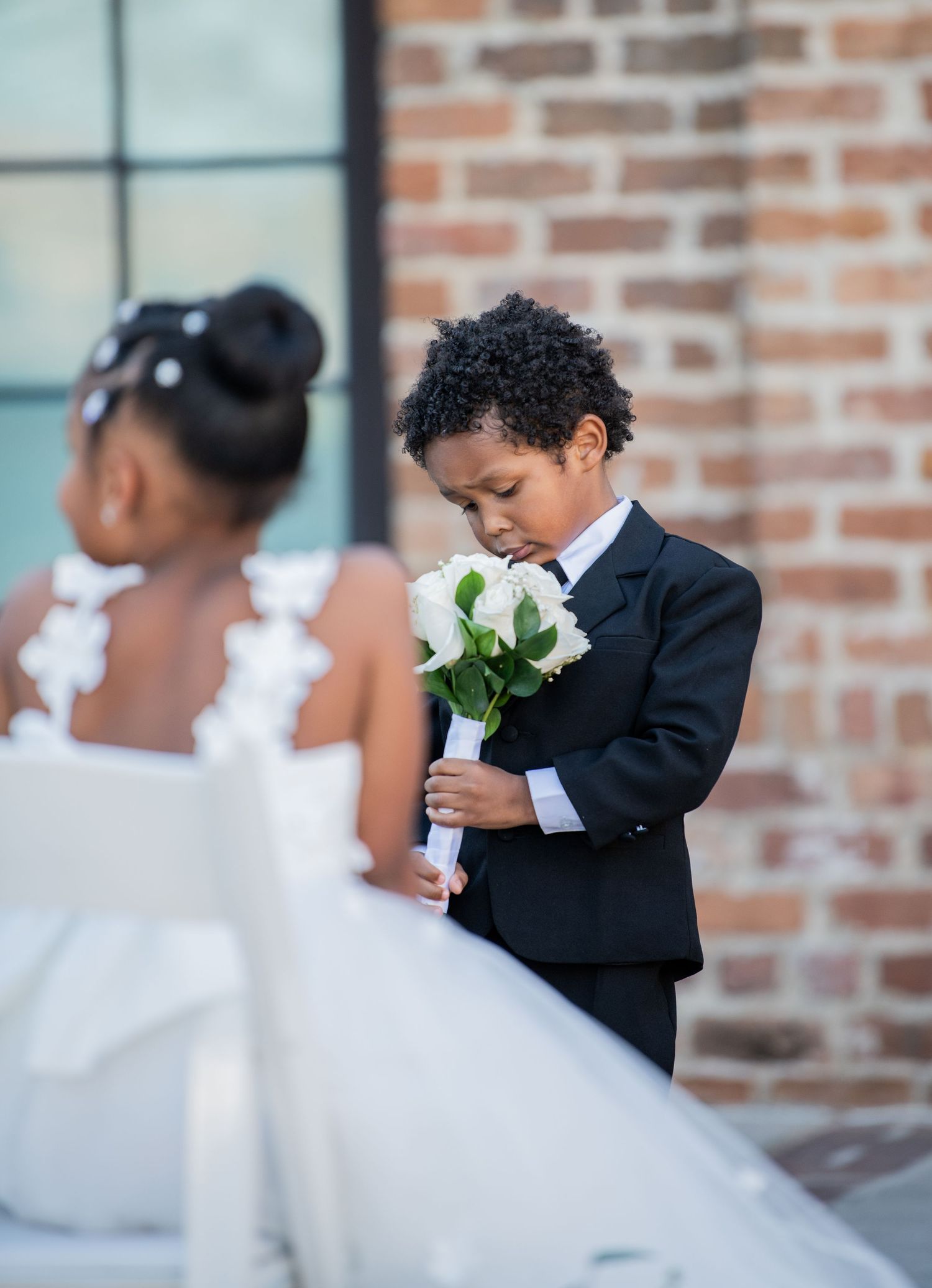 Young attendant in formal suit holding white roses at outdoor wedding.