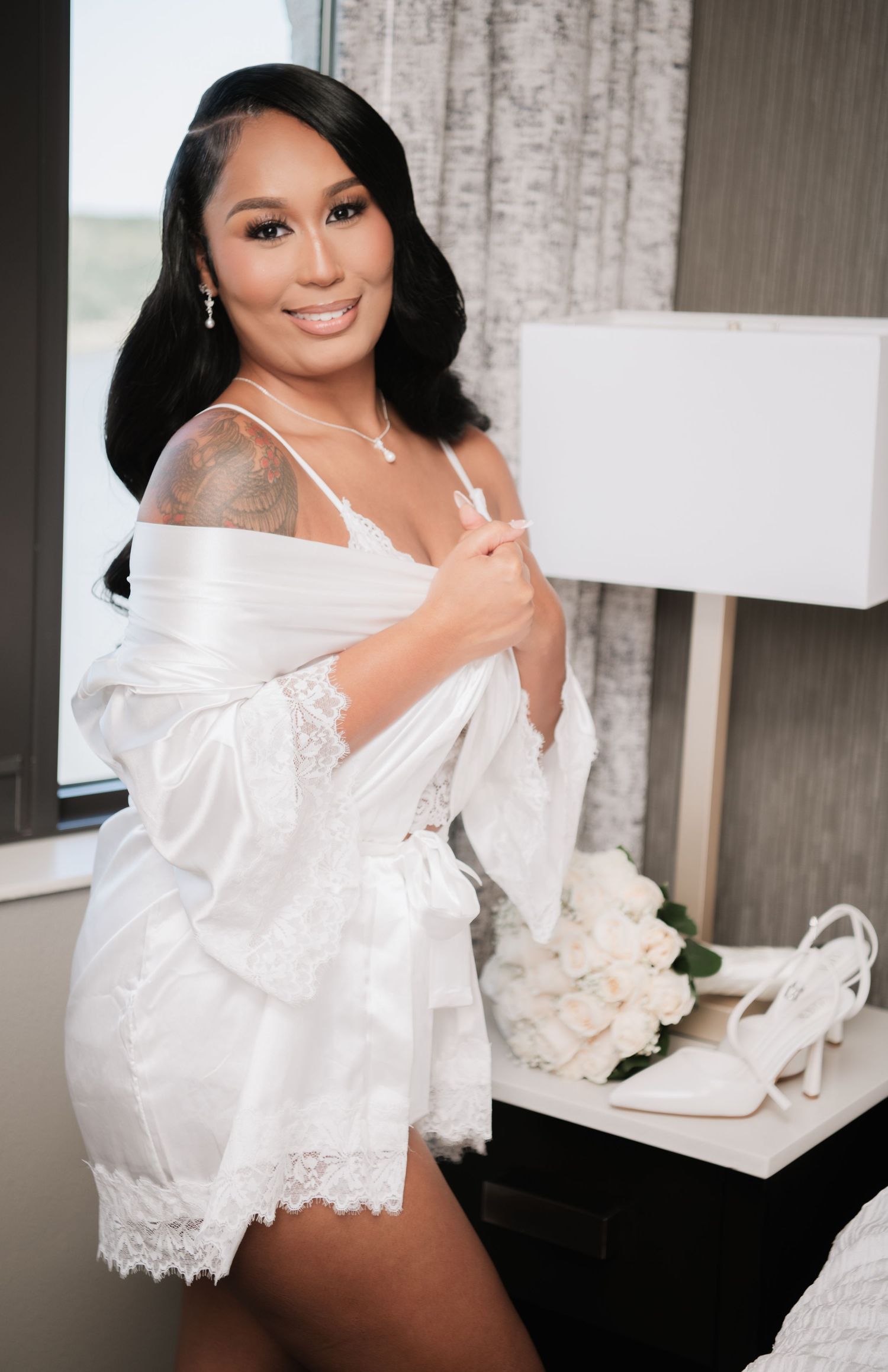 Intimate bridal getting-ready moment with white lace robe and roses.