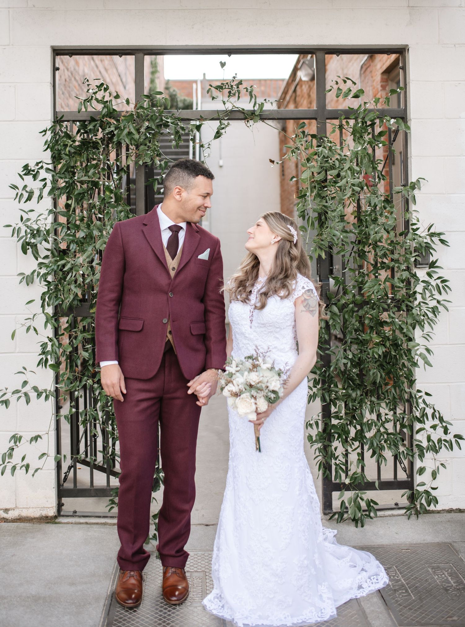 A couple shares a joyful moment in front of a greenery-adorned archway.
