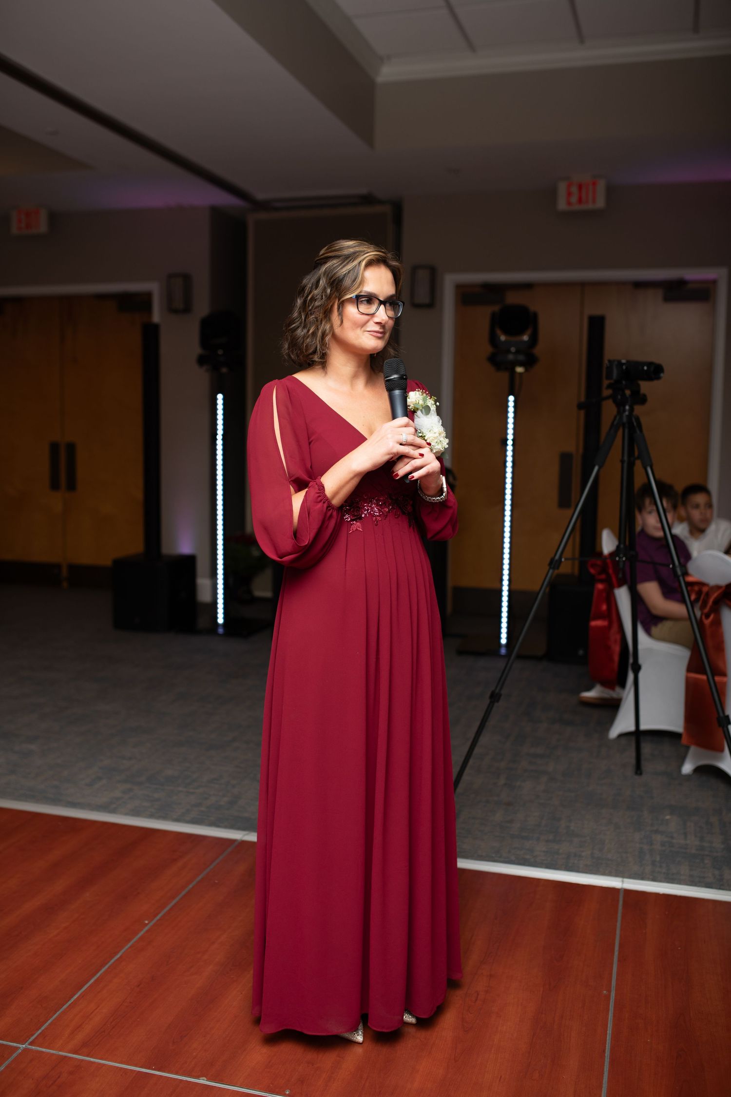 Person in a burgundy formal dress standing on a wooden dance floor.