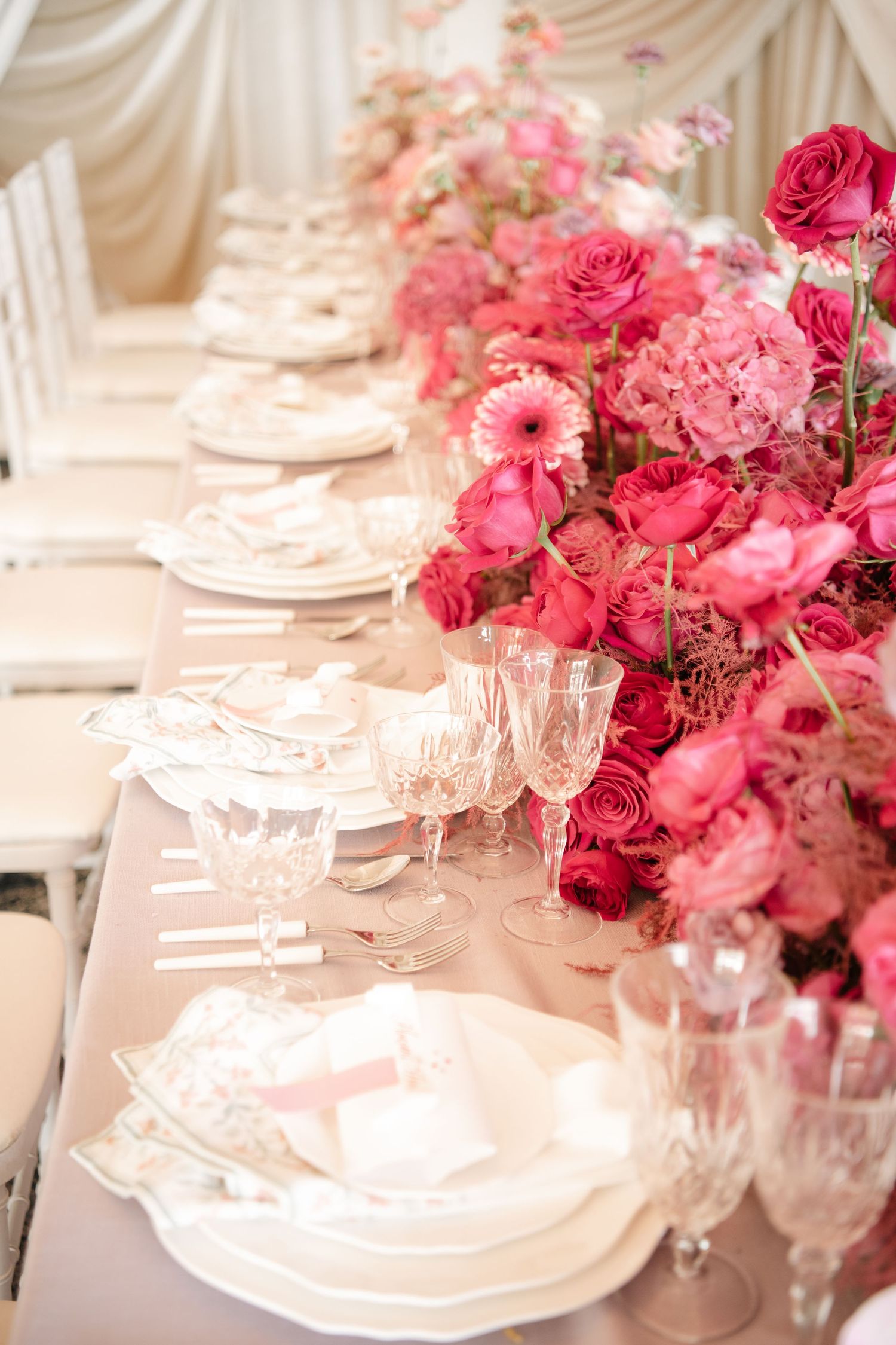 Elegant wedding table setting with pink roses and crystal glassware on white tablecloth.