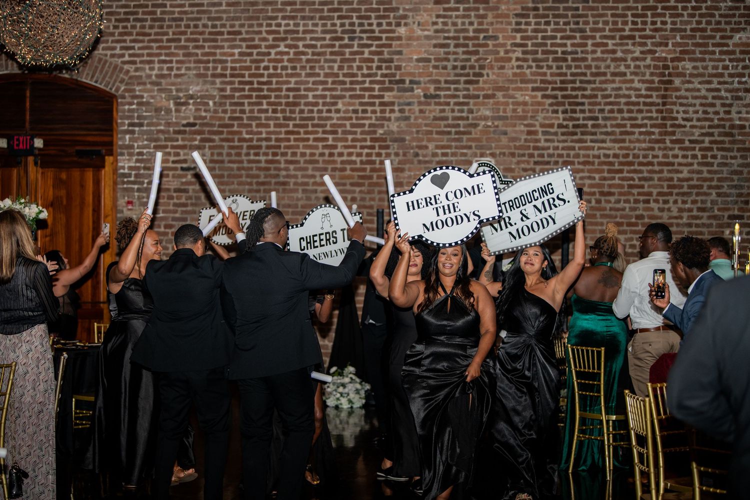 Wedding party holding up celebratory signs while dancing at reception venue.