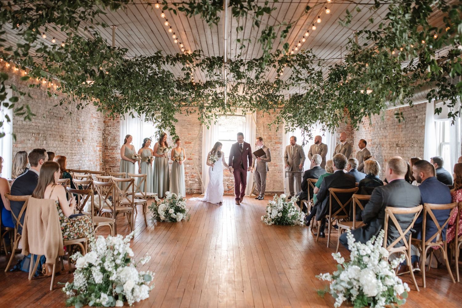 Wedding reception hall decorated with hanging greenery and white floral arrangements.
