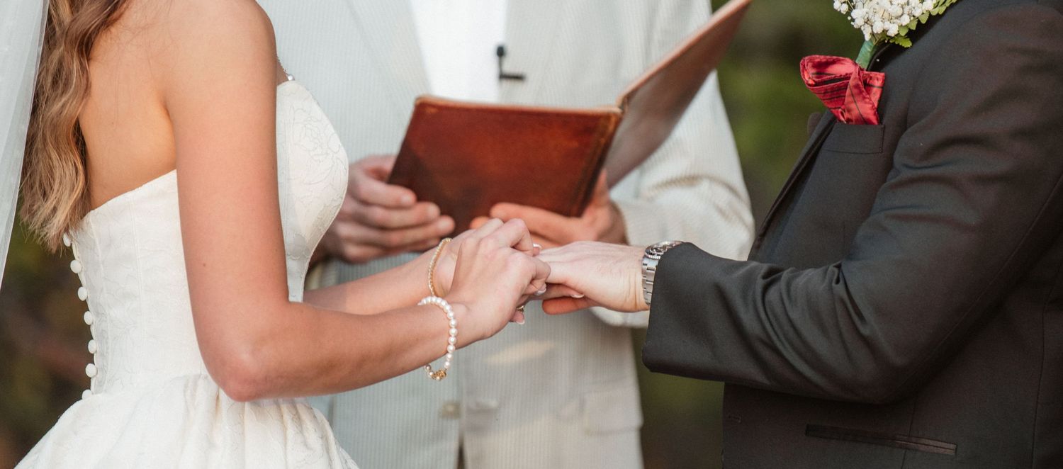 Close-up details of a white wedding dress and formal attire during an outdoor ceremony.