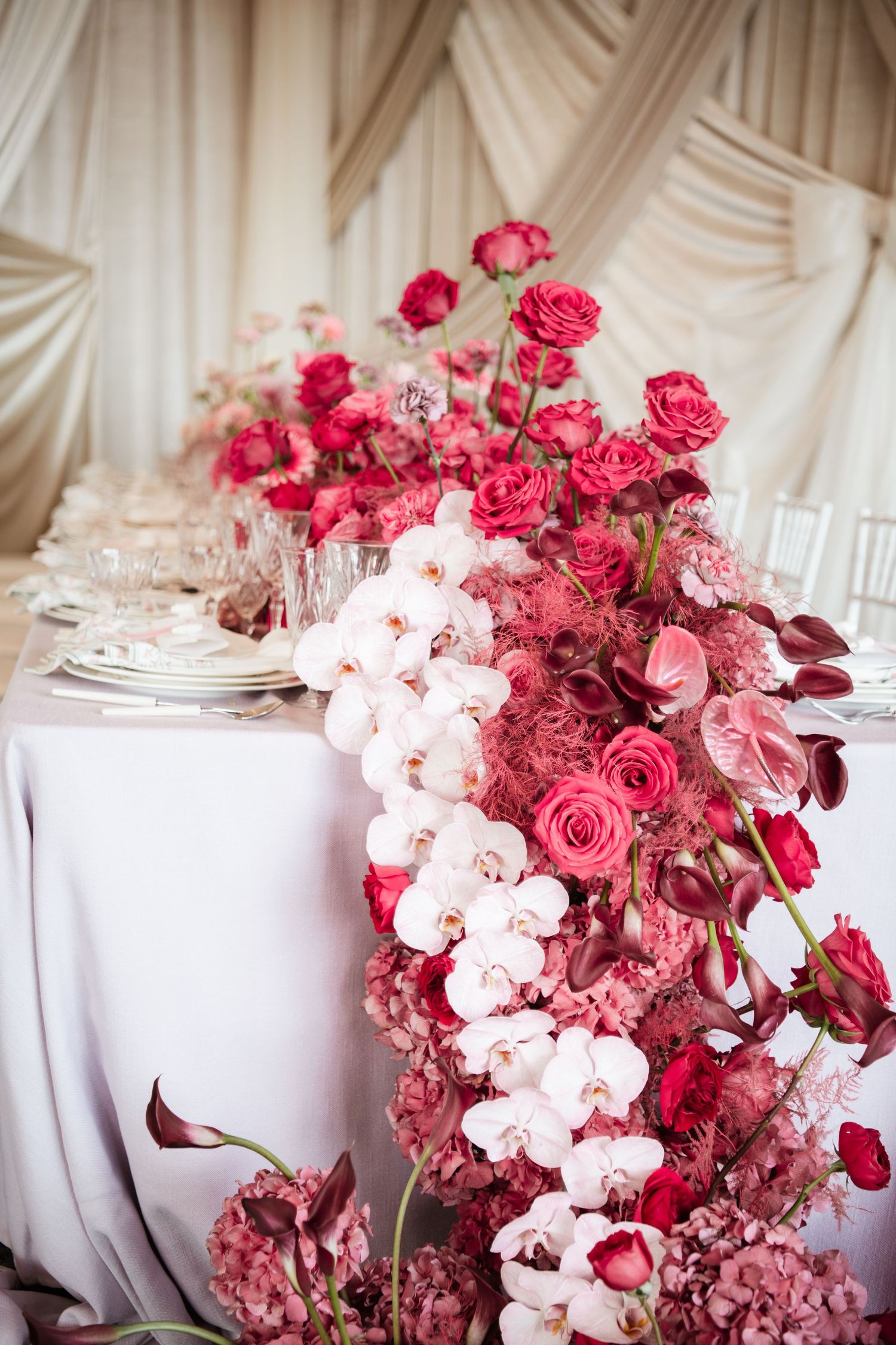 Luxurious wedding table with cascading pink roses and white orchids on draped tablecloth.