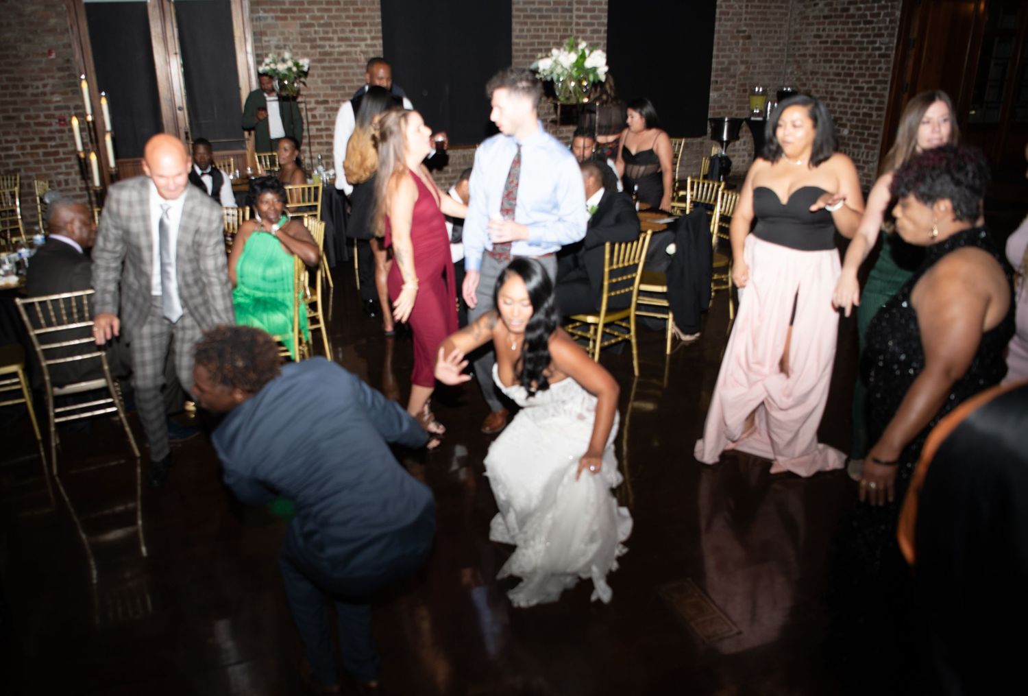 Wedding reception guests dancing and celebrating in an industrial-style venue with exposed brick walls.