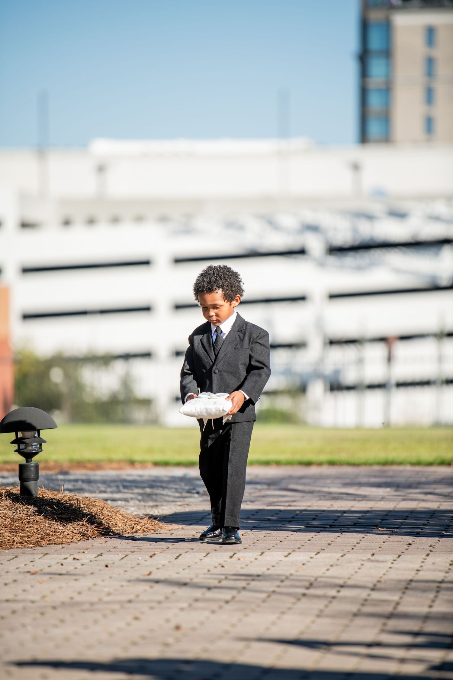 Young ring bearer in formal suit playing on stone pavers during wedding.