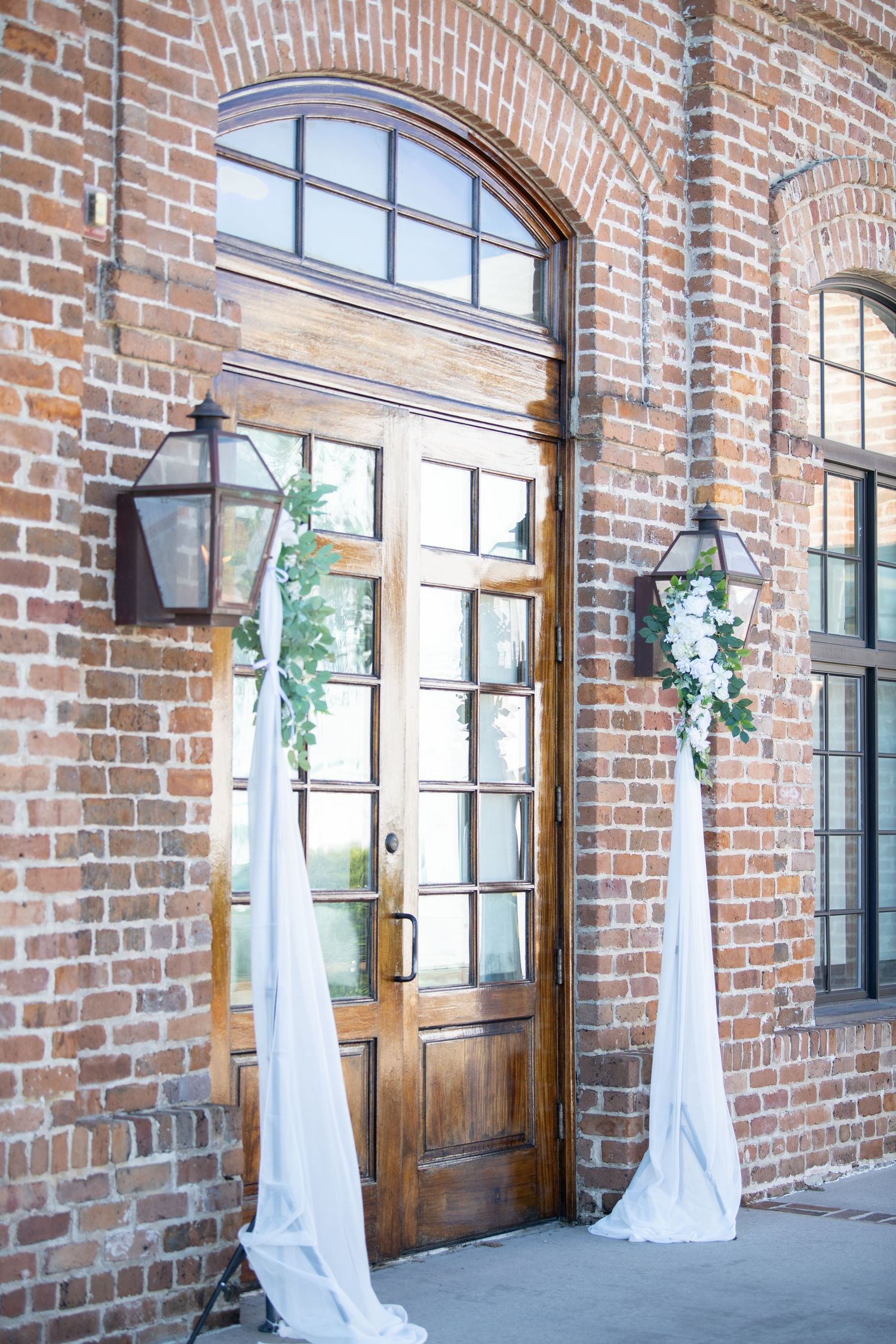 White fabric drapes elegantly frame wooden doors against exposed brick walls.