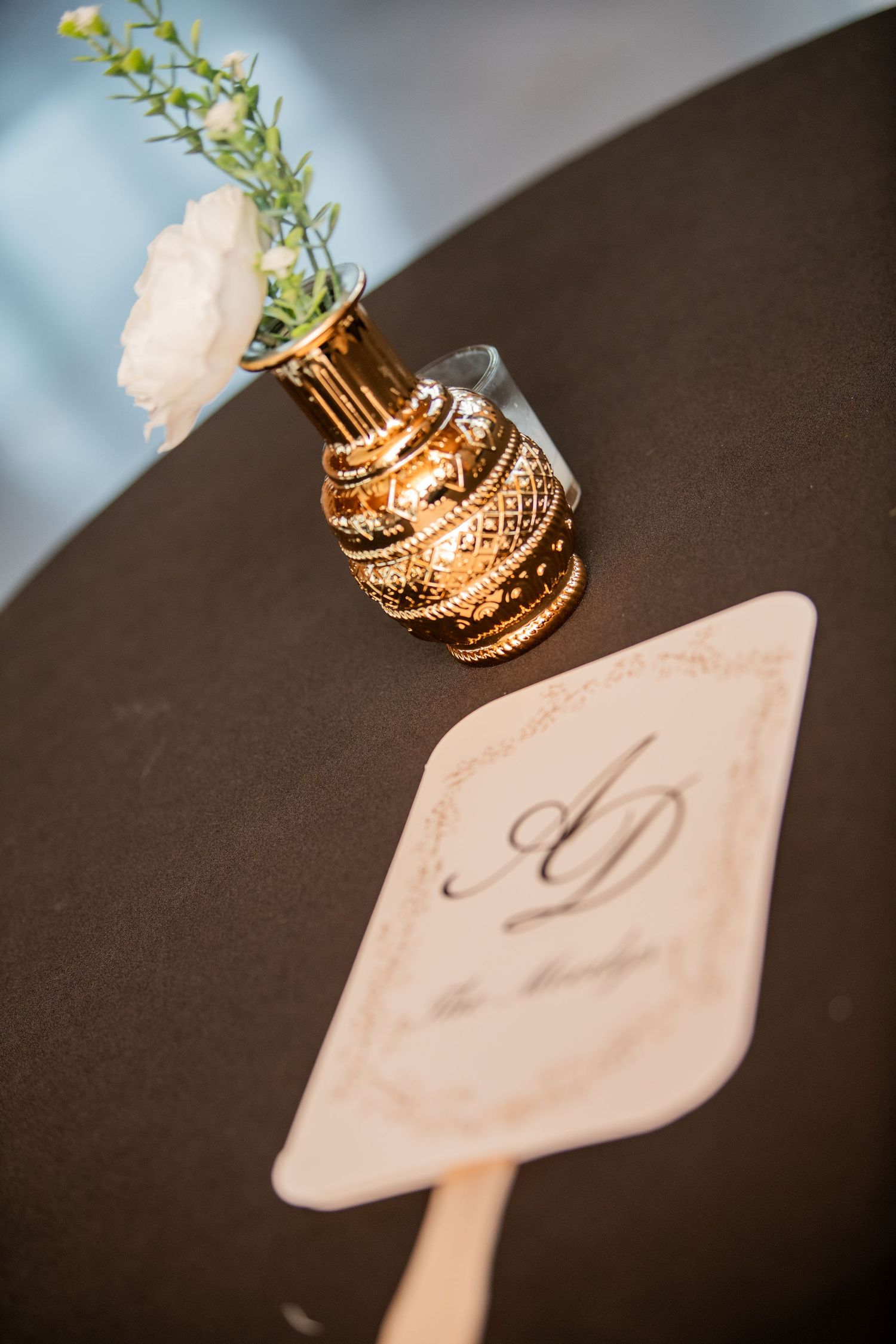Decorative gold vase with white flower and wedding monogram detail on black table.