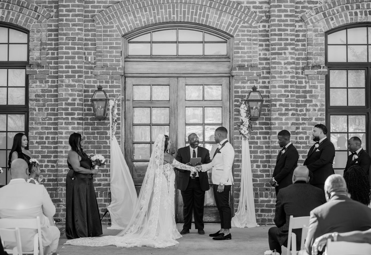 Panoramic black and white wedding ceremony shot in front of historic brick building.