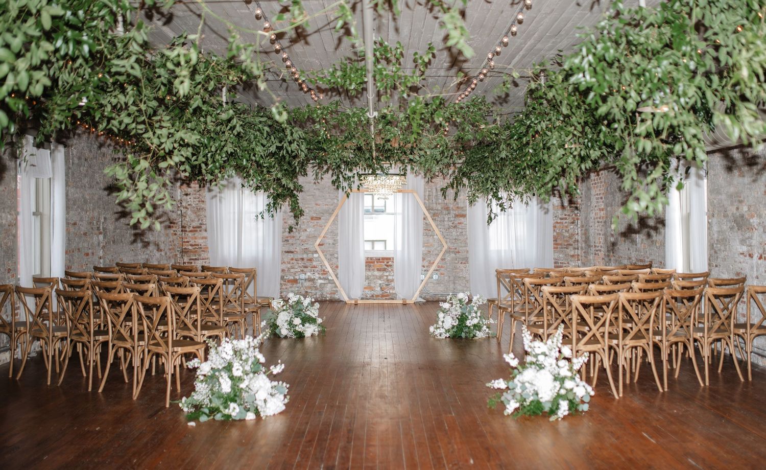 Wedding ceremony space with wooden chairs, white floral arrangements, and cascading greenery.