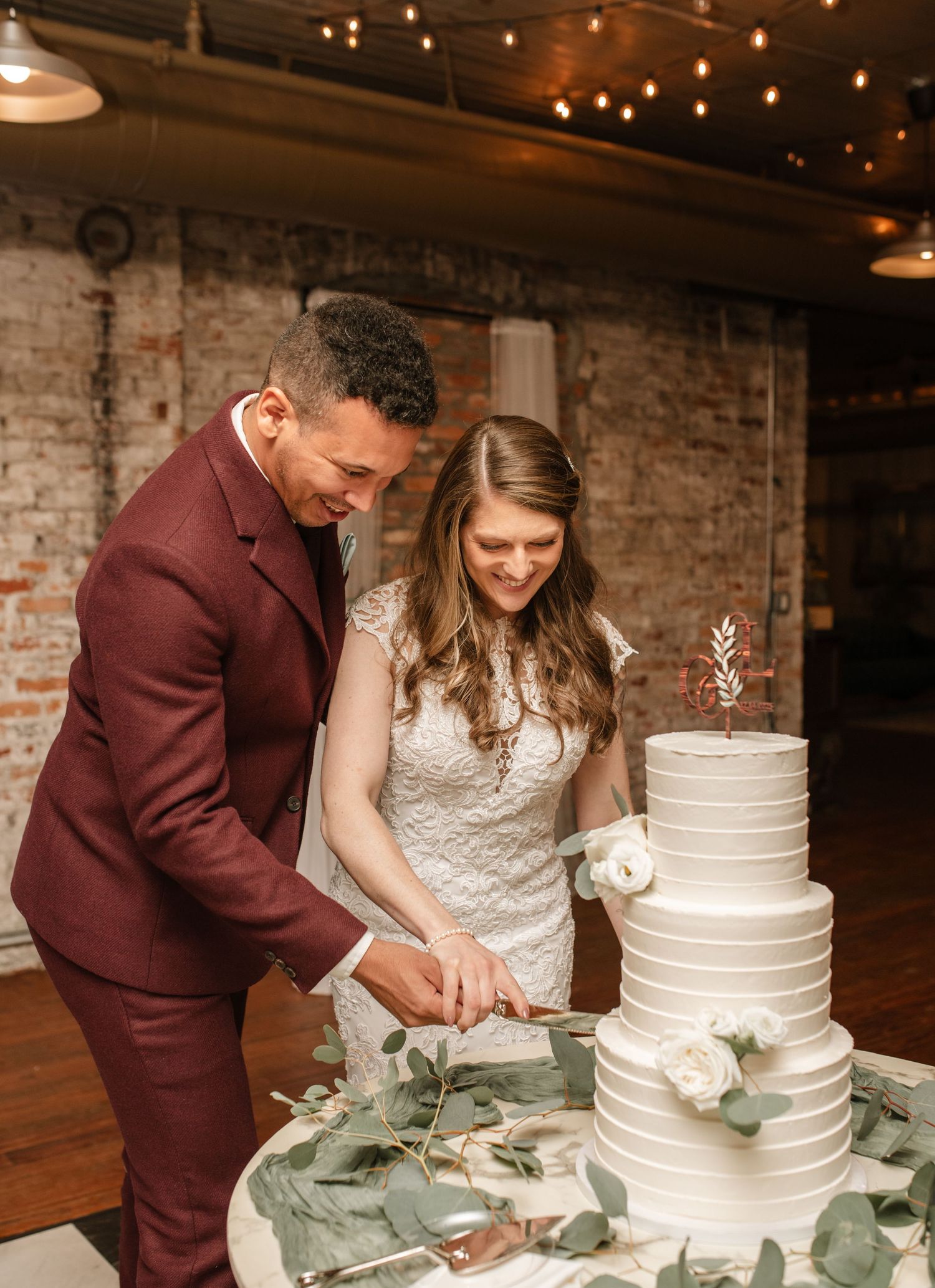 Couple cutting their white tiered wedding cake decorated with eucalyptus.
