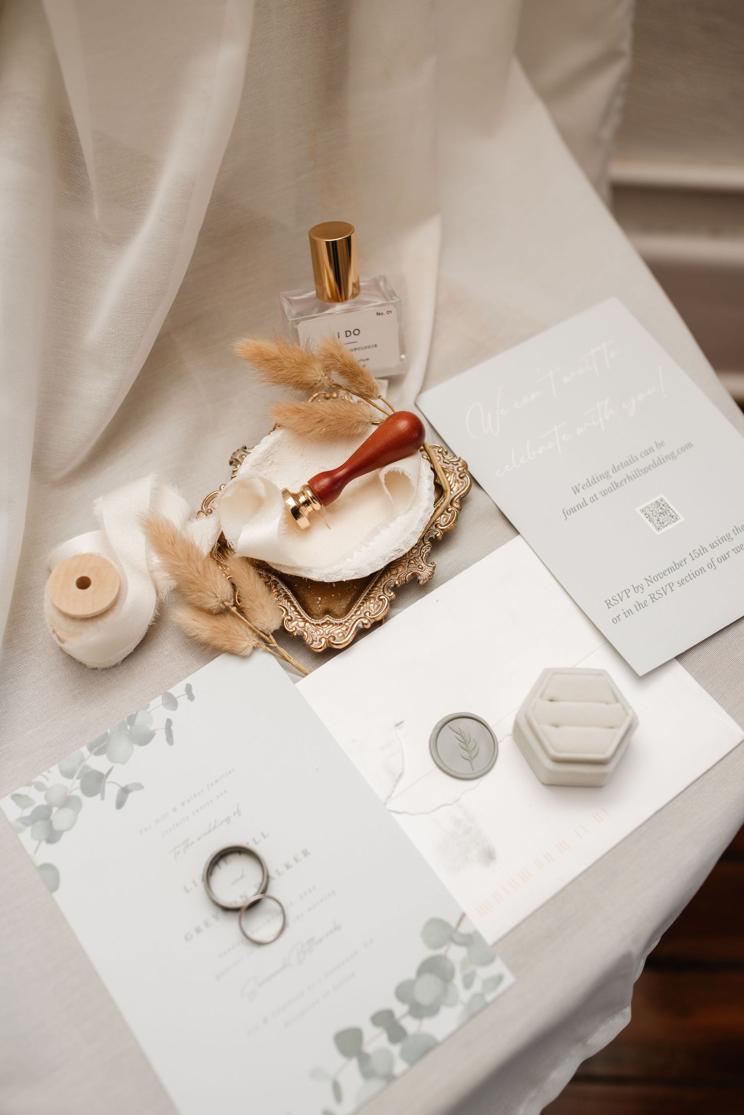 Wedding details flatlay with invitations, rings, and delicate accessories on white surface.