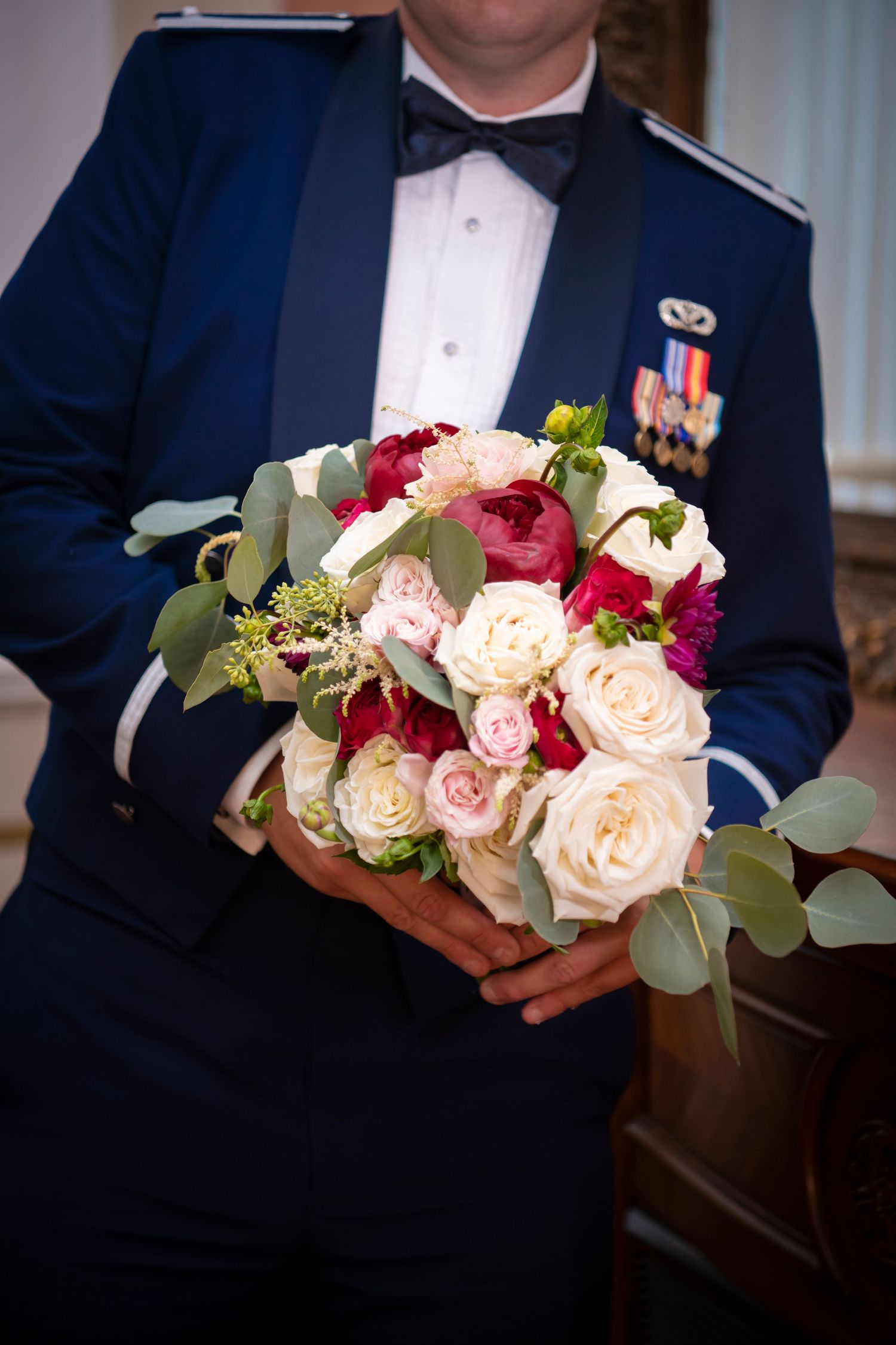 Wedding bouquet featuring blush roses and eucalyptus held by person in navy suit.