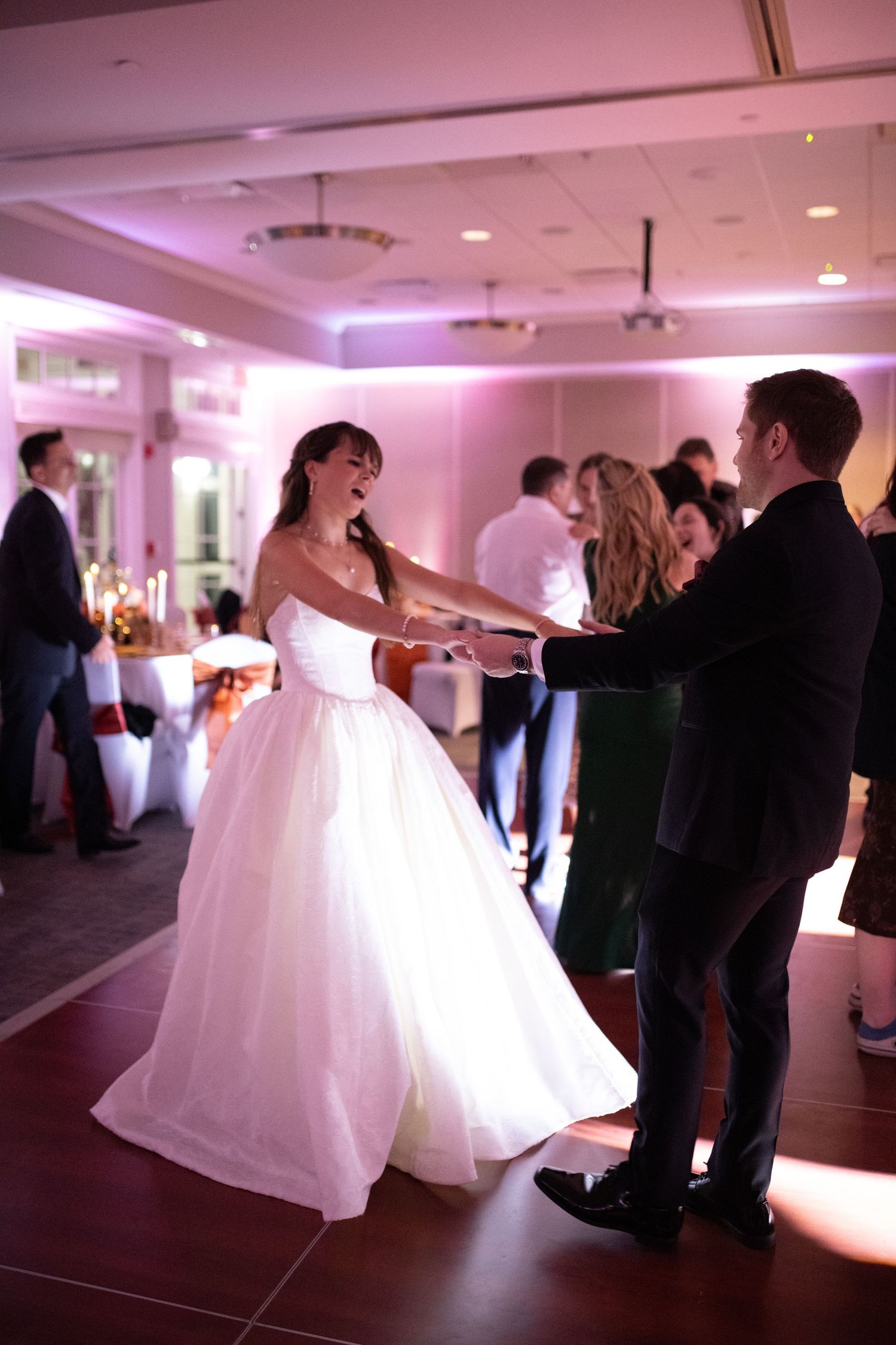Bride in flowing white gown dances with partner during romantic wedding reception in elegant ballroom.
