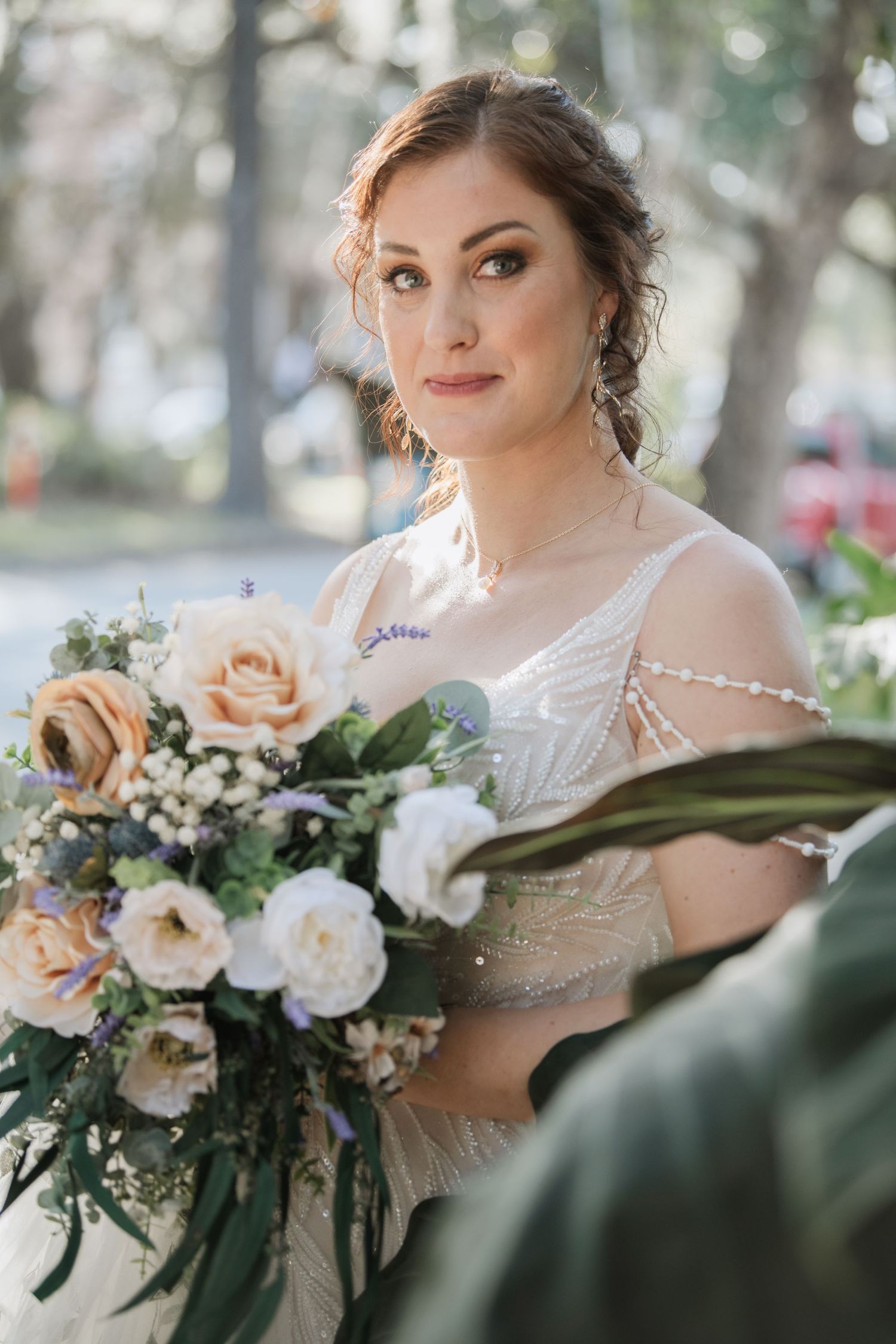 Bride wearing an ornate lace dress poses with her floral bouquet in a garden setting.